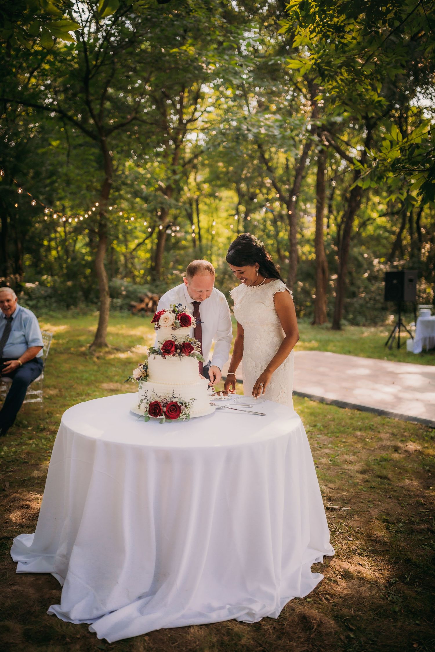 Couple completing marriage paperwork at an outdoor wedding reception surrounded by trees and string lights.
