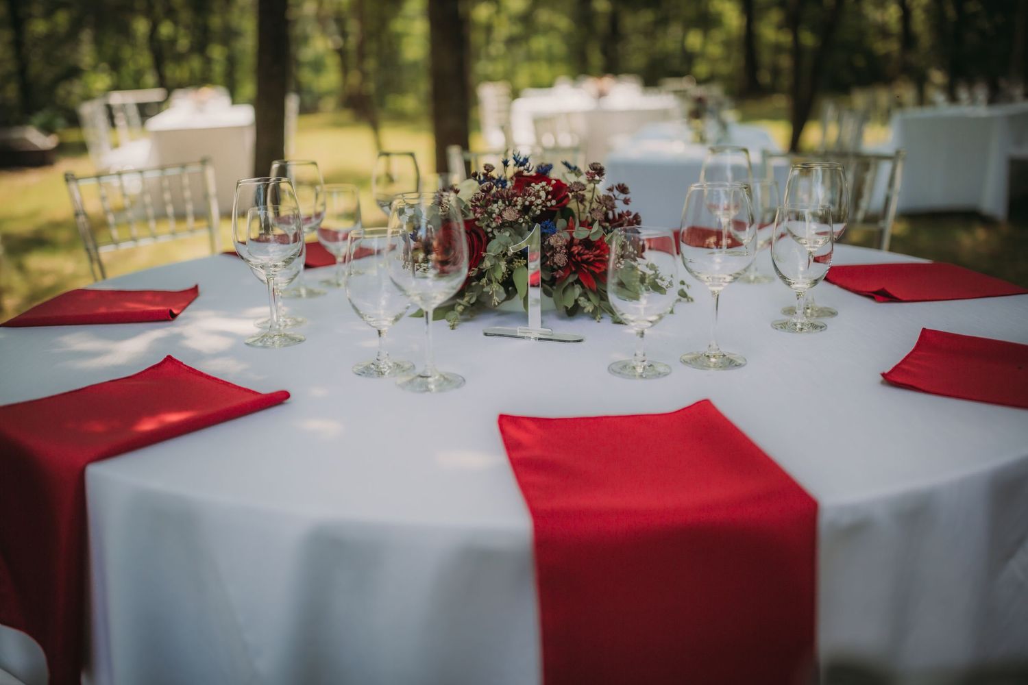 Round reception table with white tablecloth and red napkins featuring an elegant floral centerpiece.