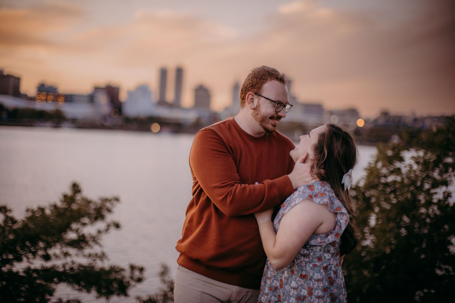 Tender embrace between couple with urban waterfront and sunset sky backdrop.