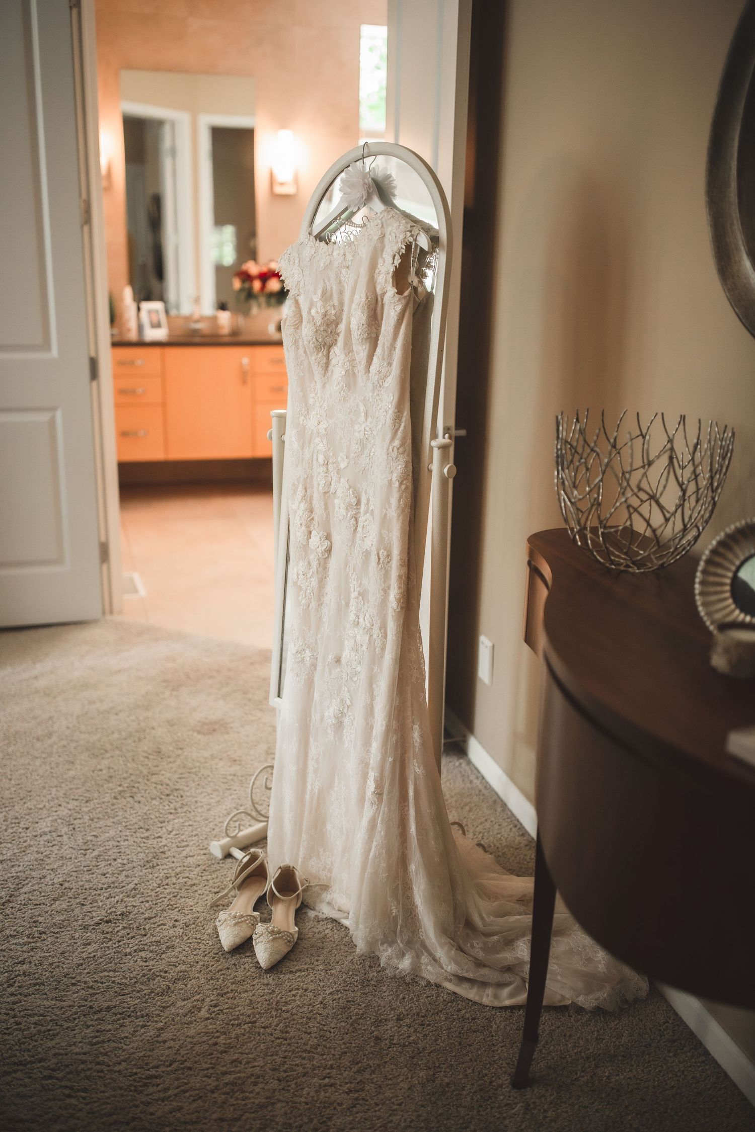Lace wedding dress hanging in a doorway with white heels placed beneath.