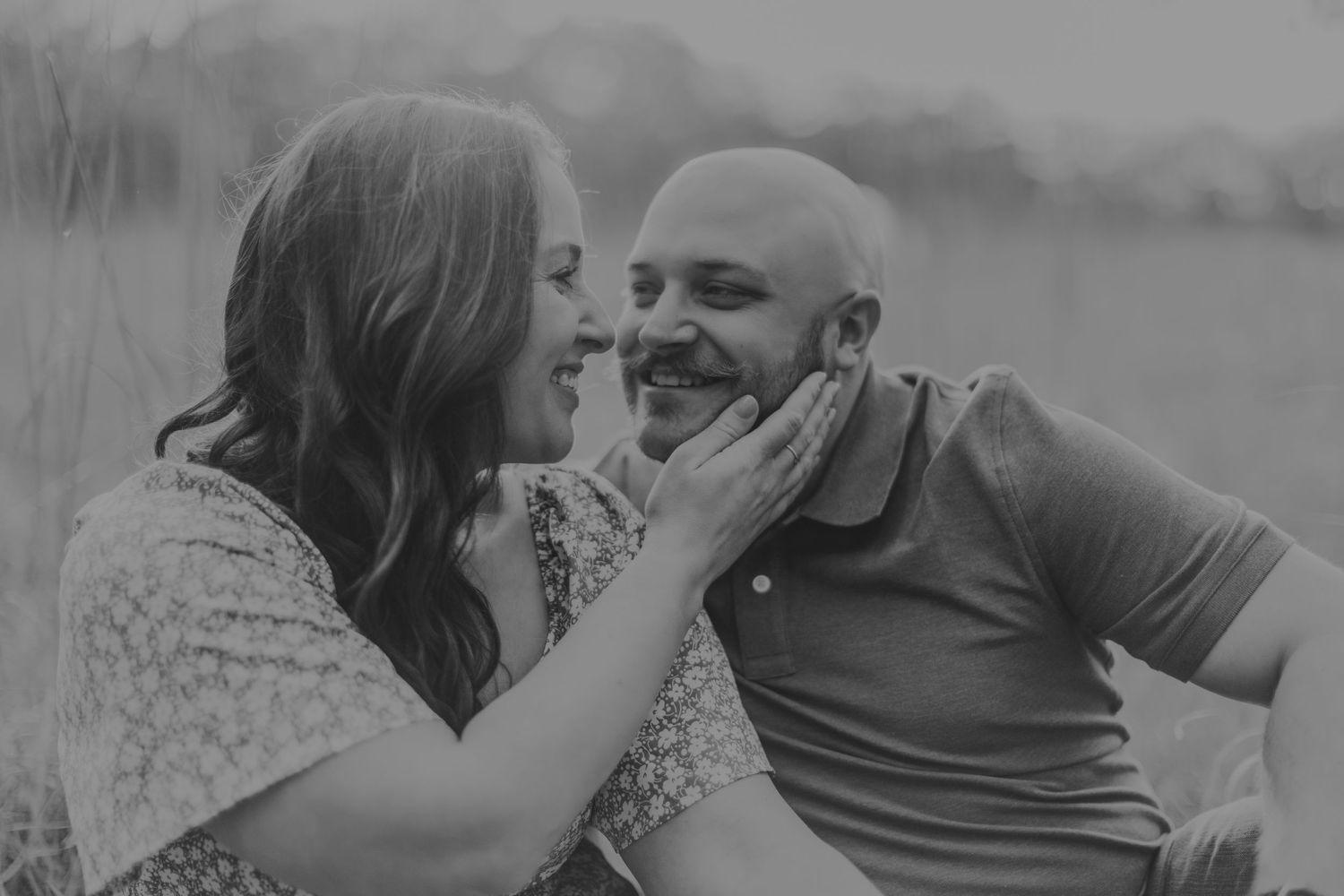A black and white image shows a couple sharing an intimate moment in nature.