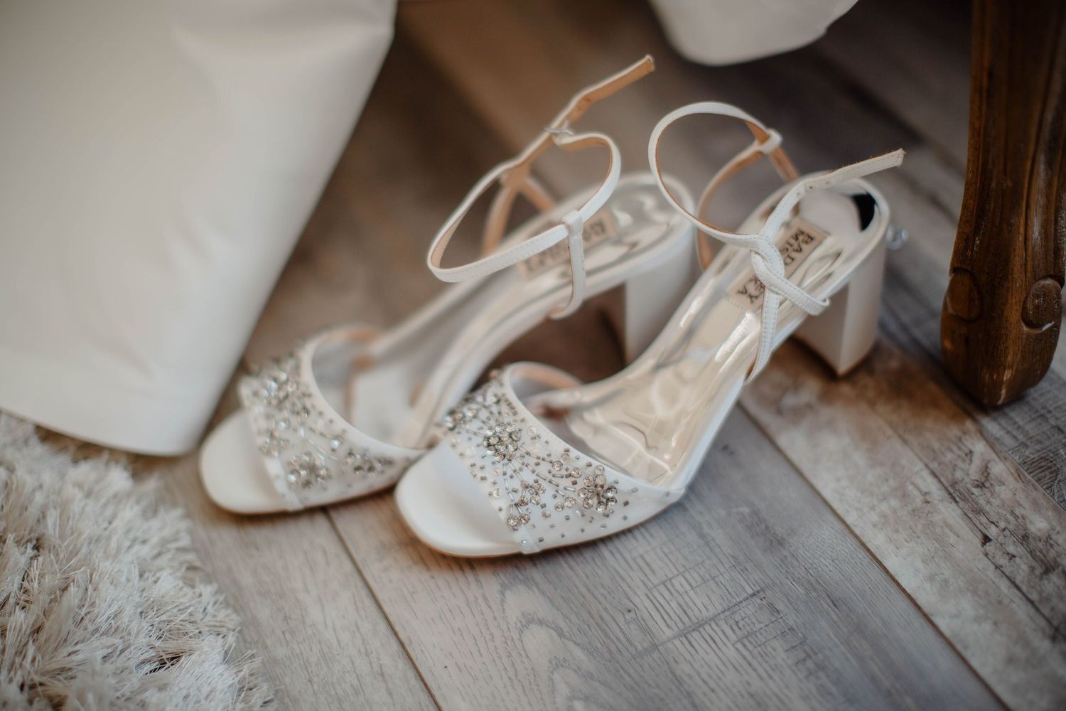 Elegant white bridal shoes with crystal embellishments on wooden floor.