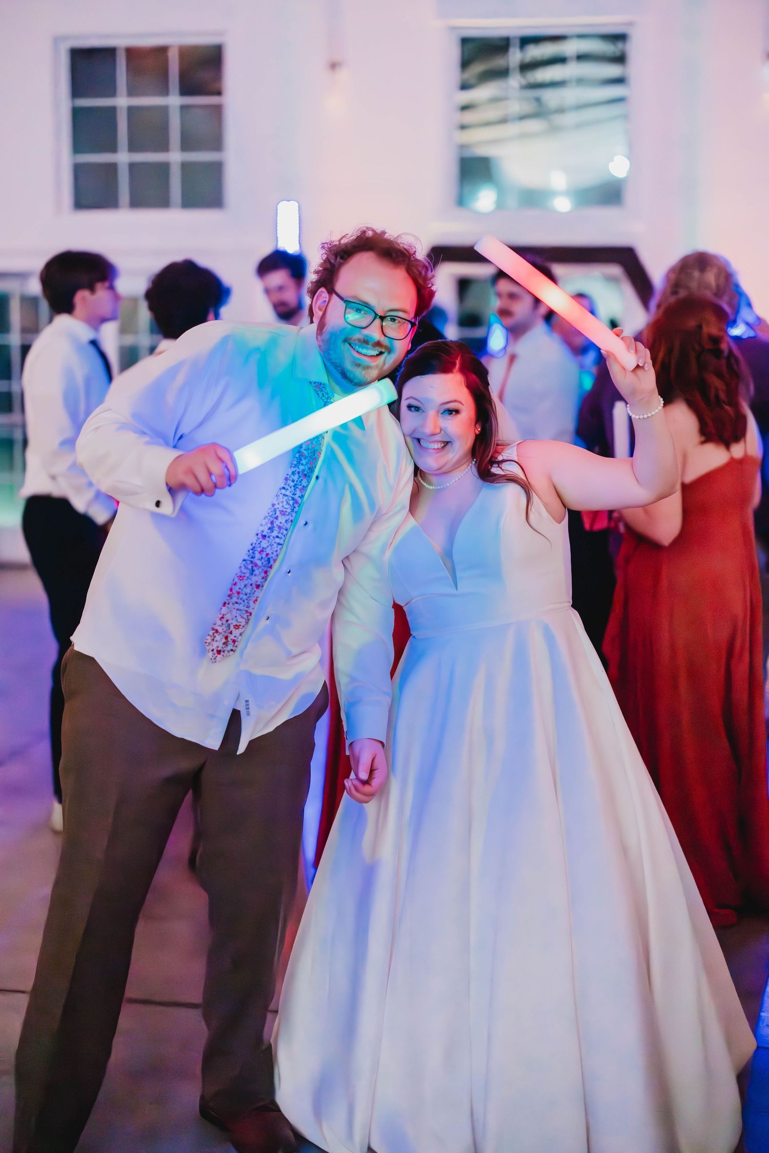 Newlyweds dance energetically with glow sticks at their wedding reception bathed in blue light.