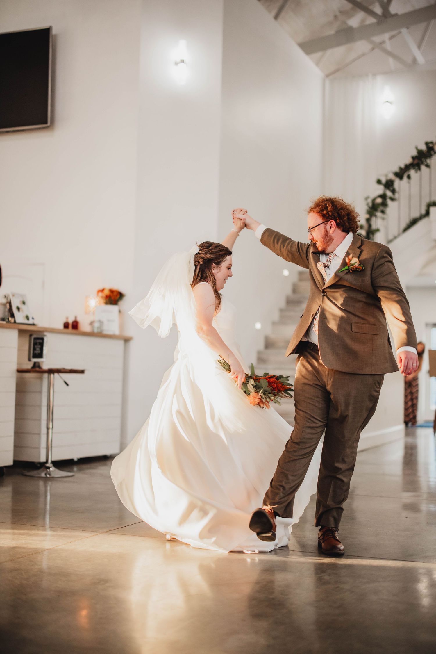 Couple performs a playful dance move during their wedding reception in a modern white venue.