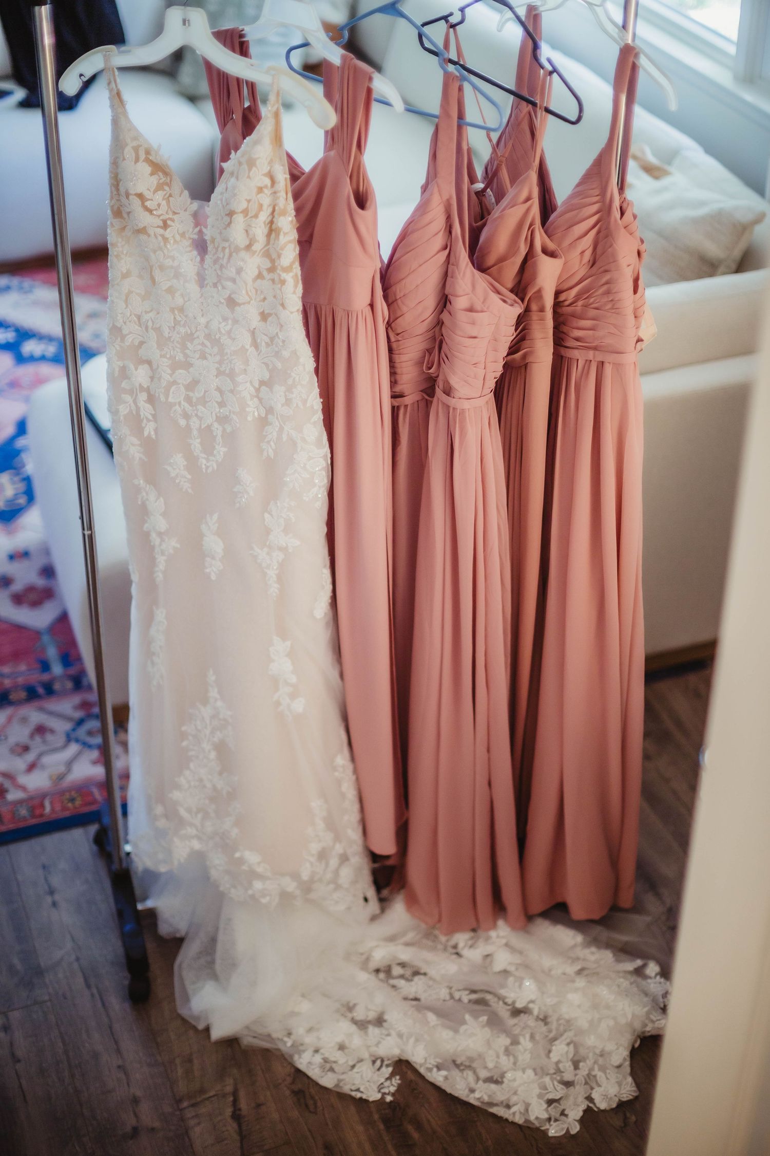 Wedding dress collection featuring a white lace gown and blush pink bridesmaid dresses on hangers.