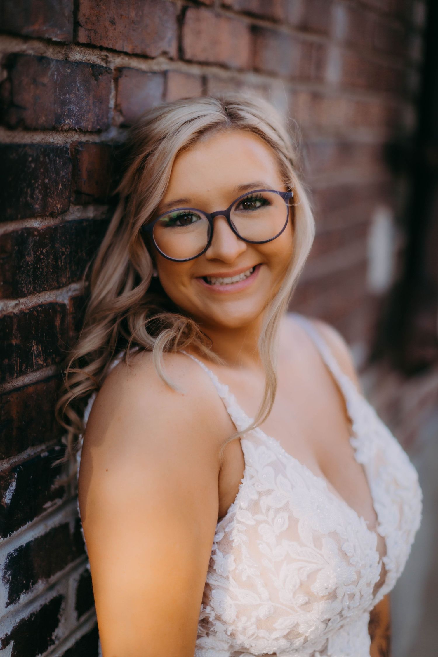 Portrait of a smiling bride wearing a white lace wedding dress and glasses.
