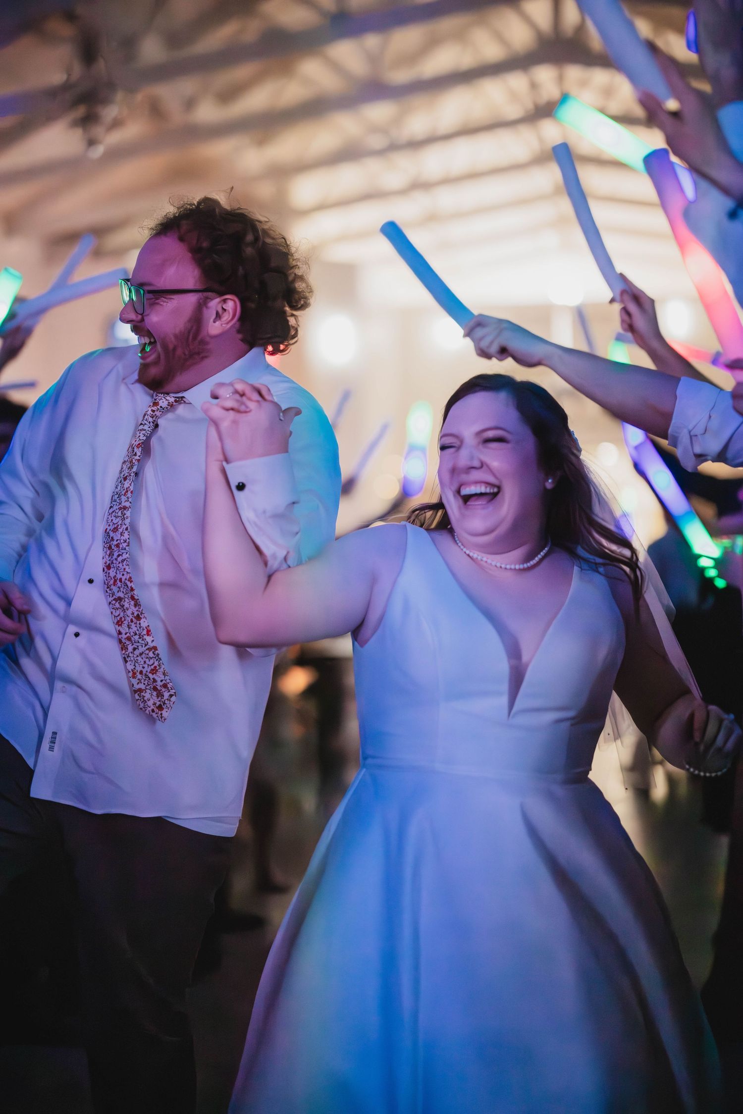 Wedding couple laughing and dancing beneath colorful glow sticks at their evening reception.