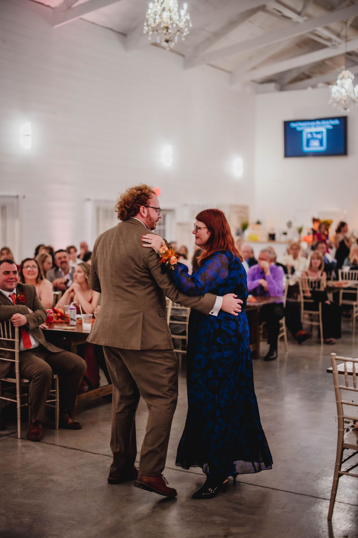A couple in formal attire dances together at a wedding reception while guests watch from their tables.