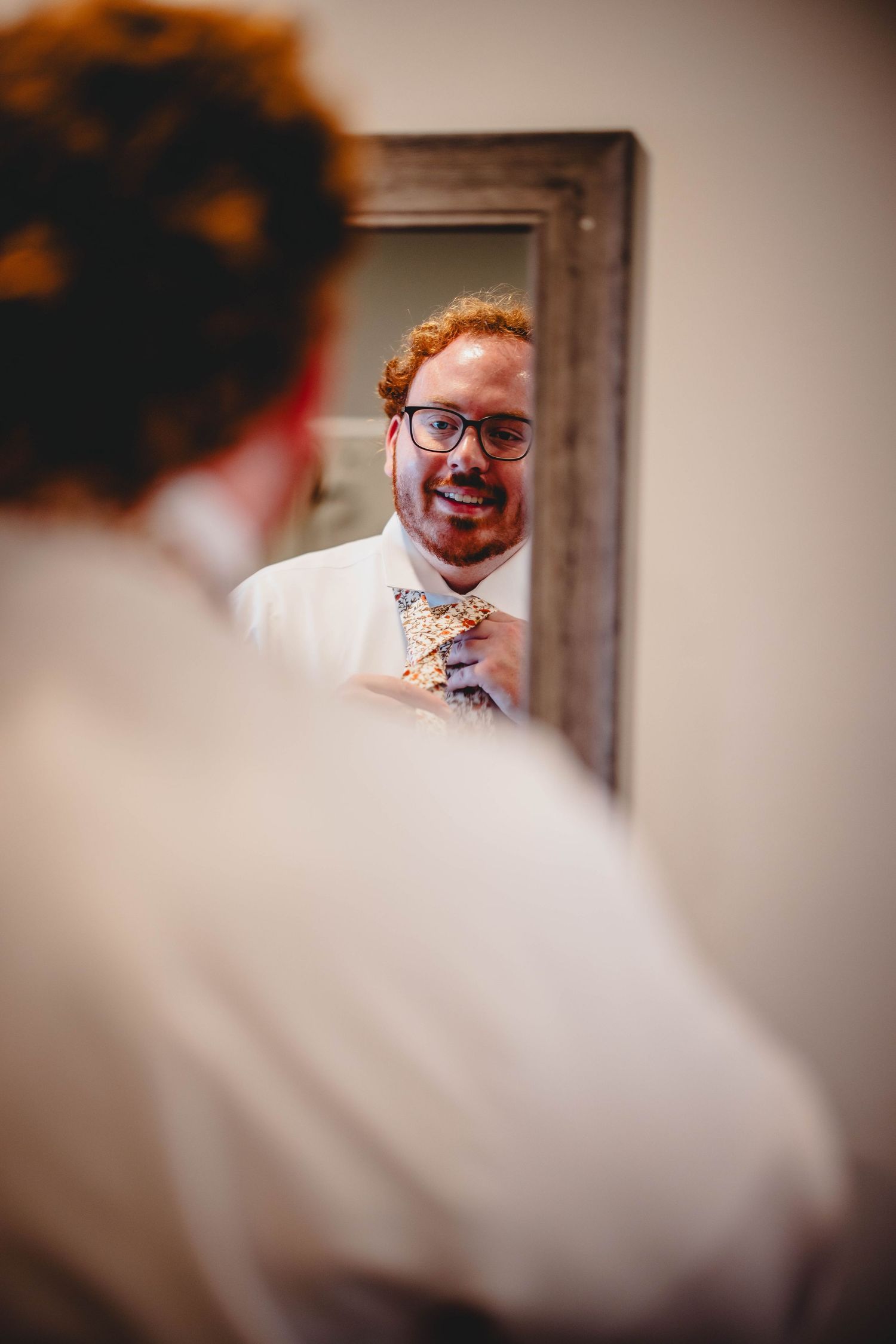 A candid mirror reflection showing someone smiling while adjusting their bowtie.