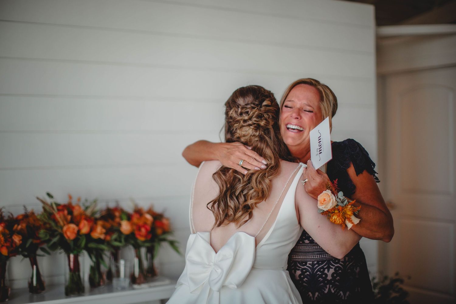 An emotional embrace shared during wedding preparations with orange flowers in background.