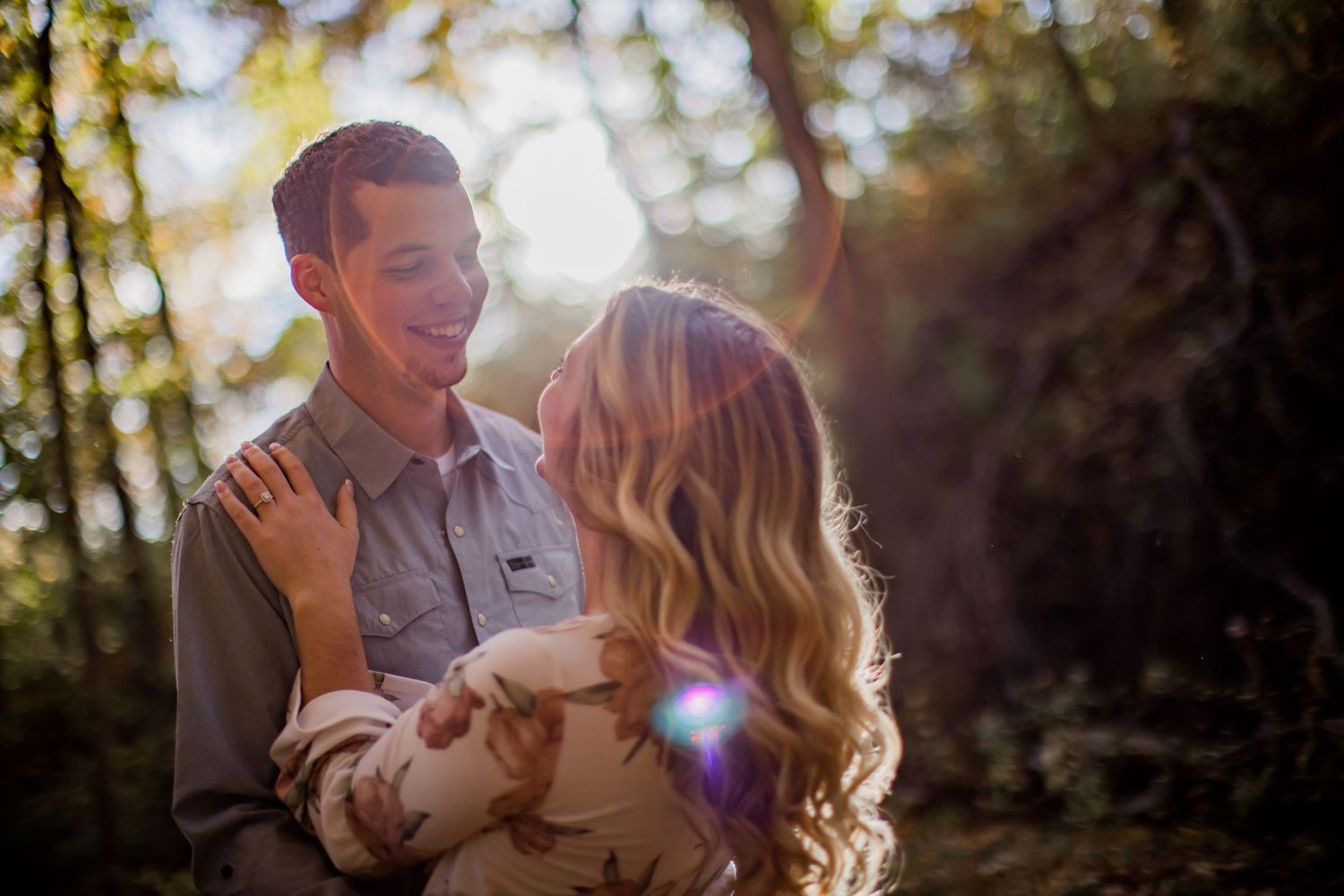 Happy couple embracing and laughing together in a sun-dappled forest setting.