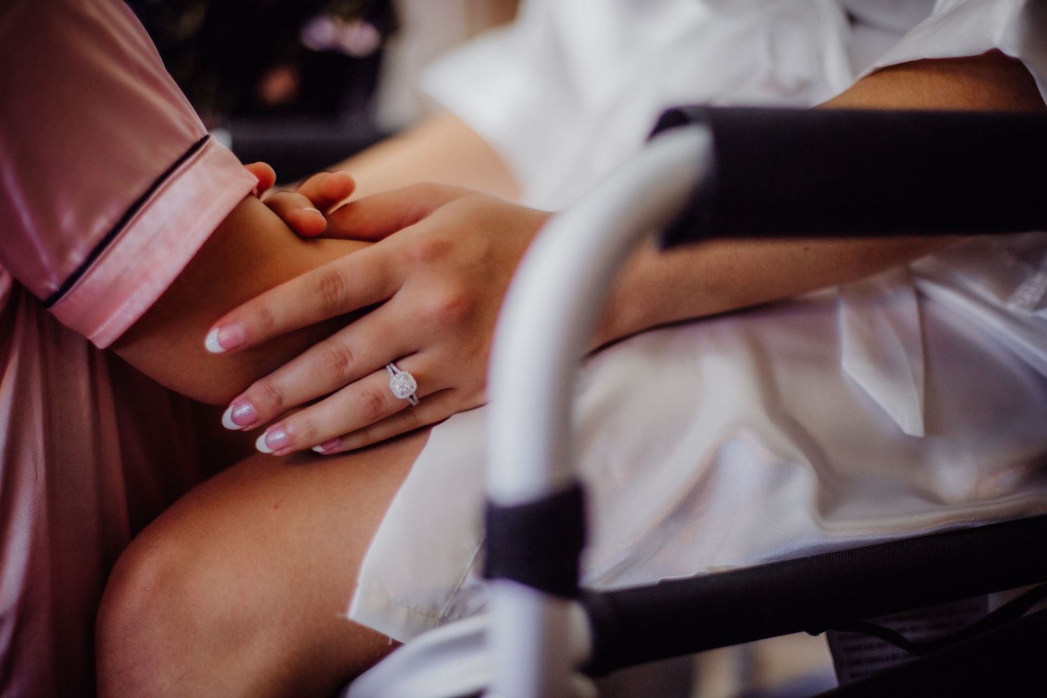 Hands with fresh manicure rest gently on white fabric during wedding preparations.