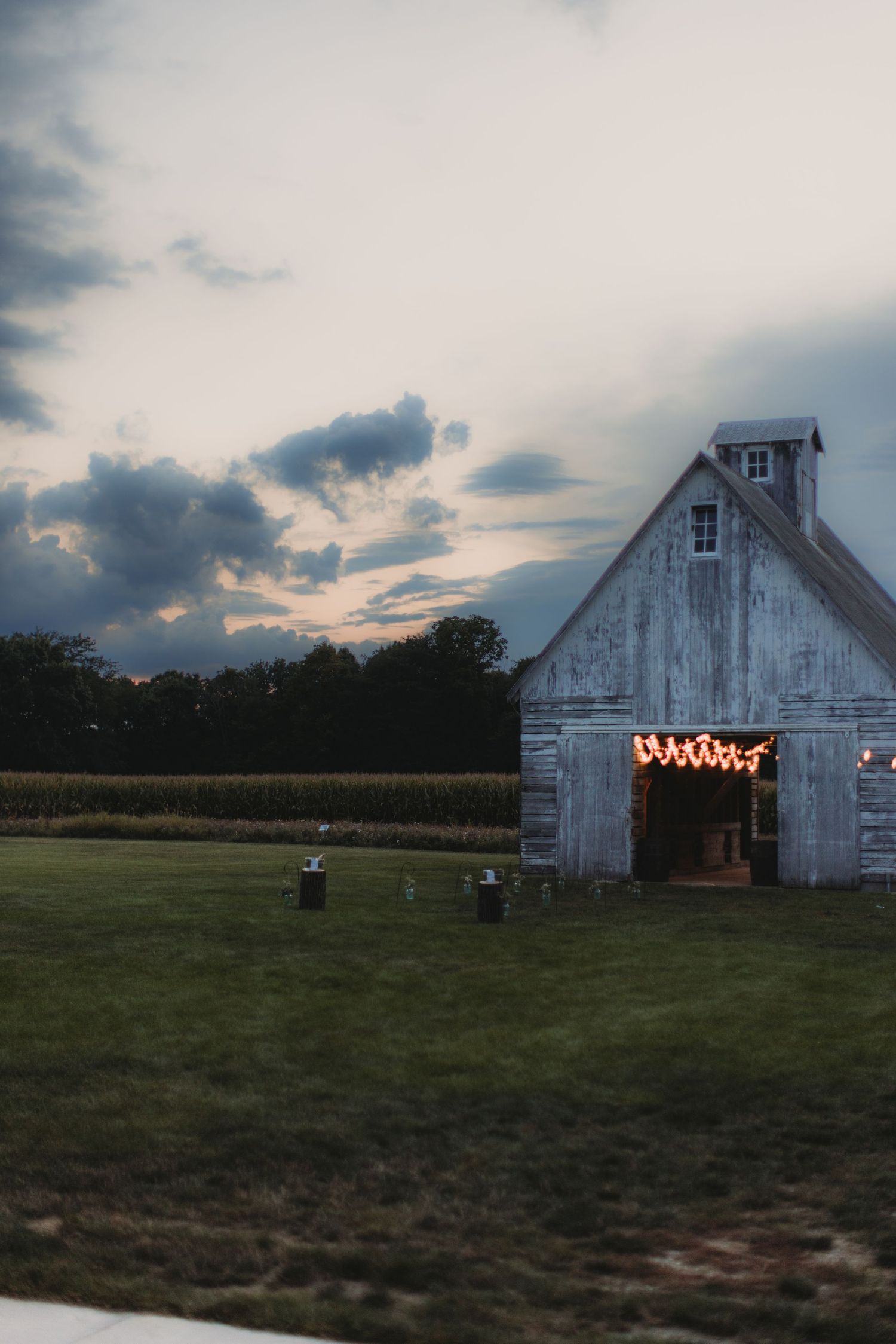 White barn illuminated with string lights at sunset creating a romantic rustic atmosphere.