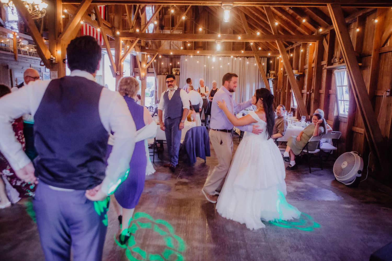 Panoramic view of a rustic barn wedding reception with dancers and ambient lighting.