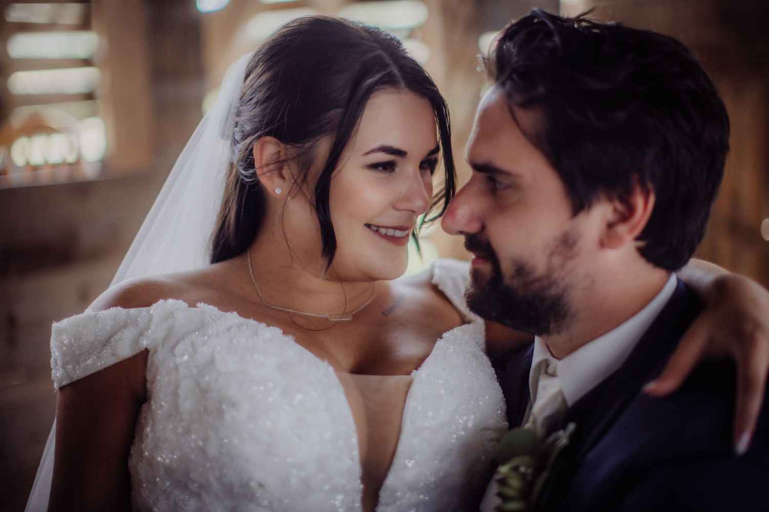 Newlyweds embrace tenderly in a rustic barn with filtered sunlight creating a romantic atmosphere.