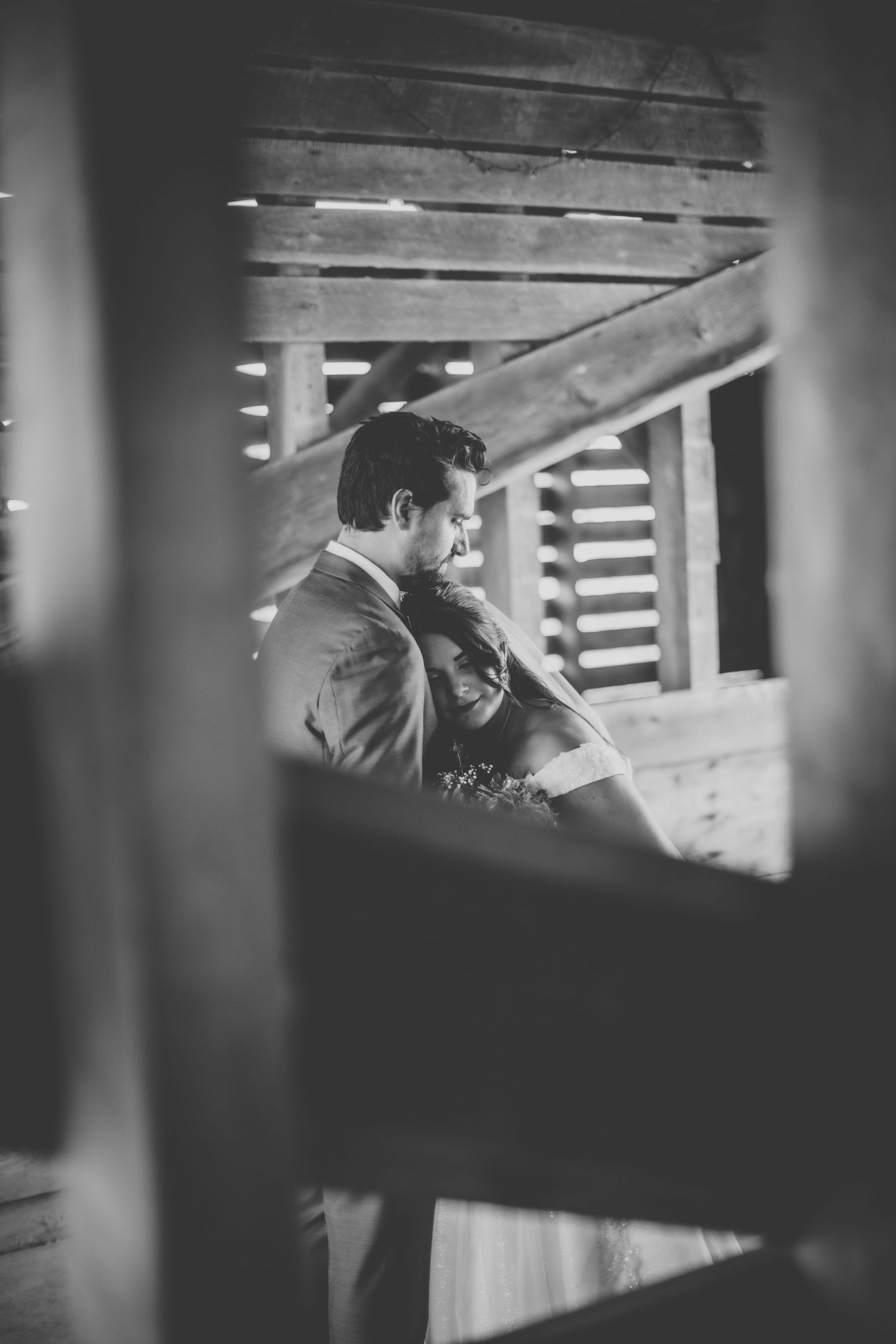 Wedding party poses in natural light by rustic barn windows for an artistic black and white photograph.