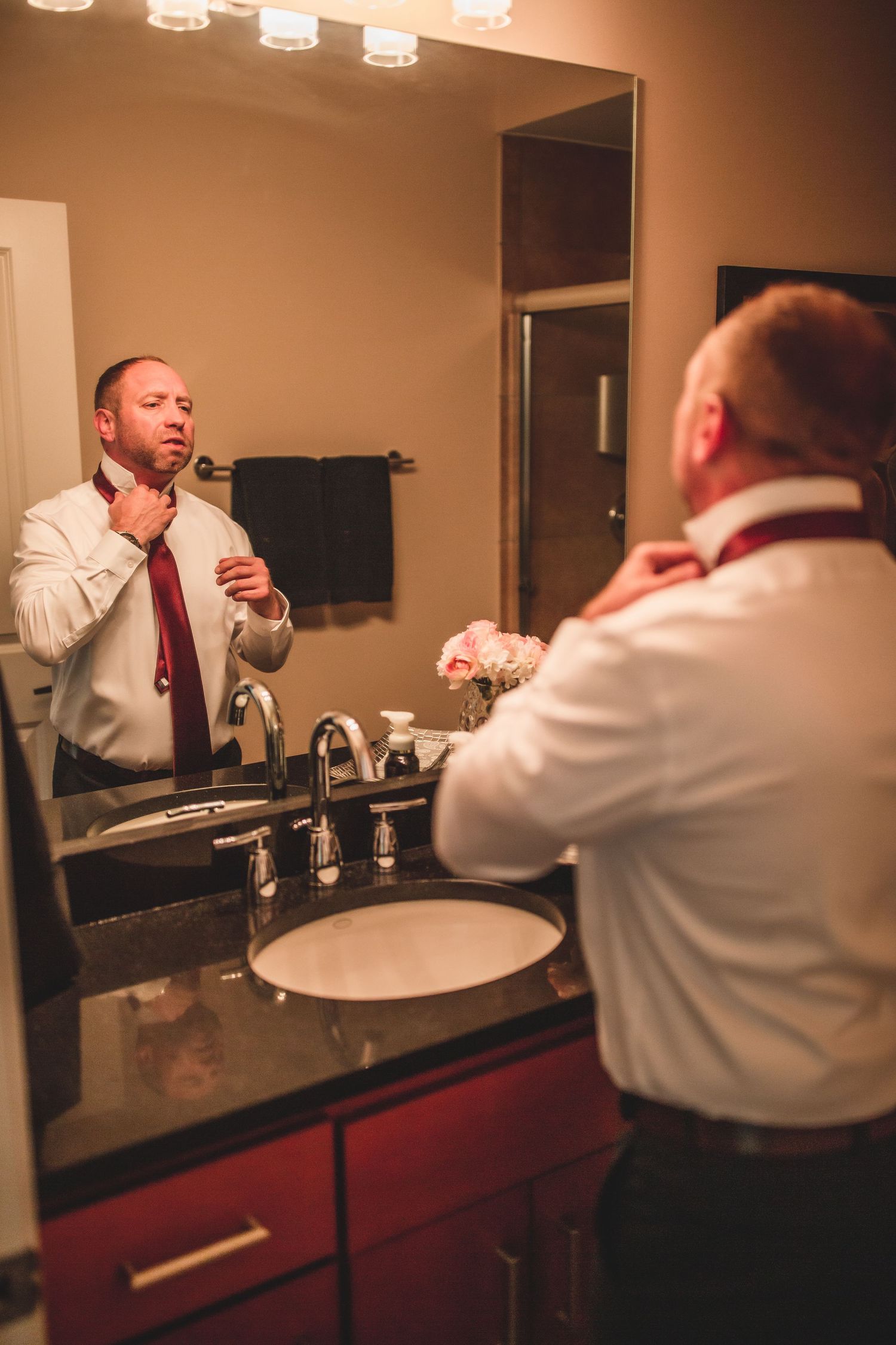 Side view of person fixing tie in front of bathroom mirror with red vanity.