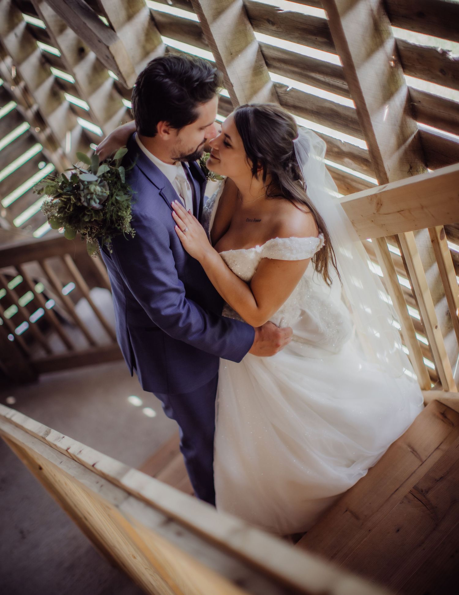 Wedding couple shares intimate moment in rustic wooden venue with streaming sunlight.