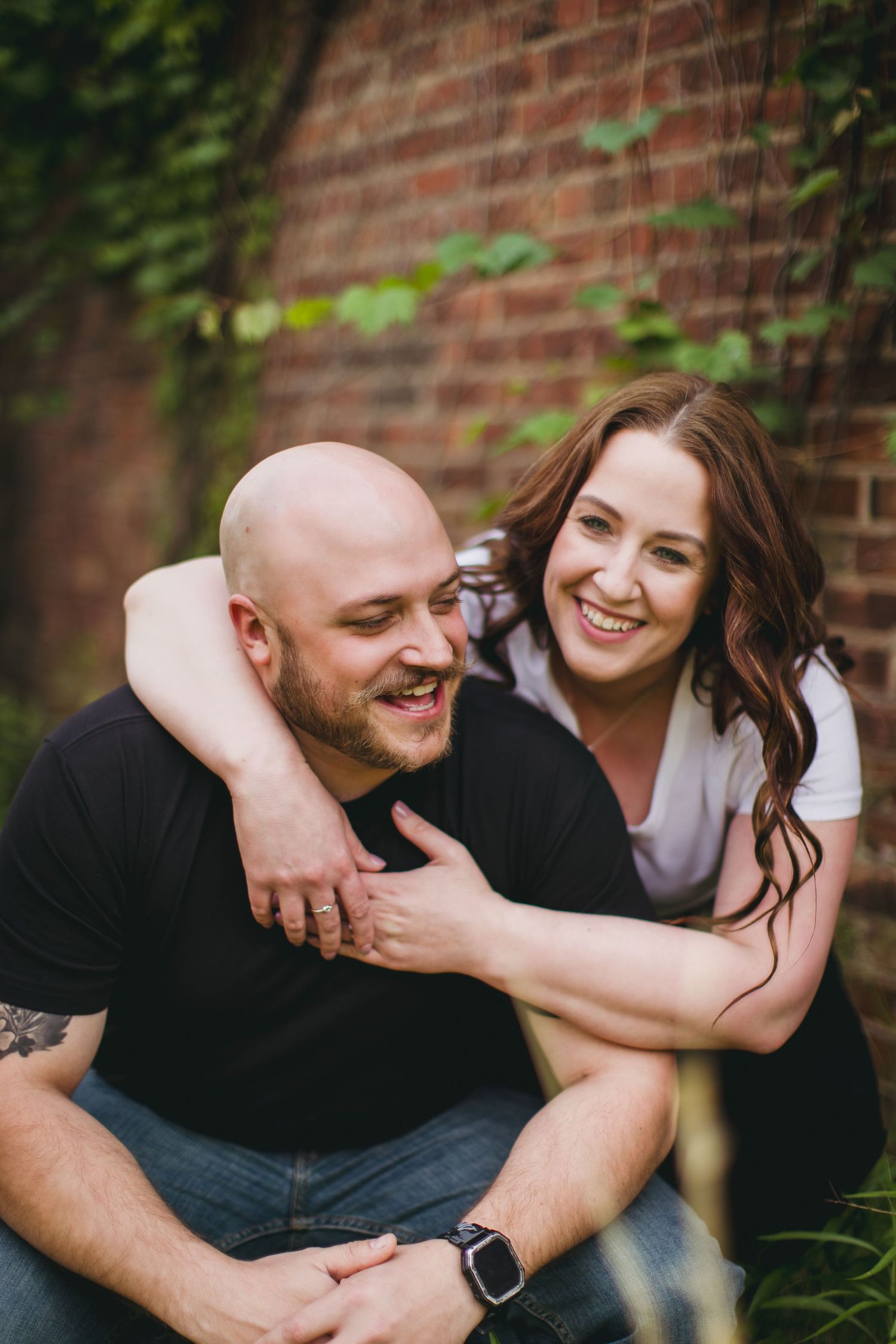 Playful engagement photos showing natural interactions between couple by brick building.