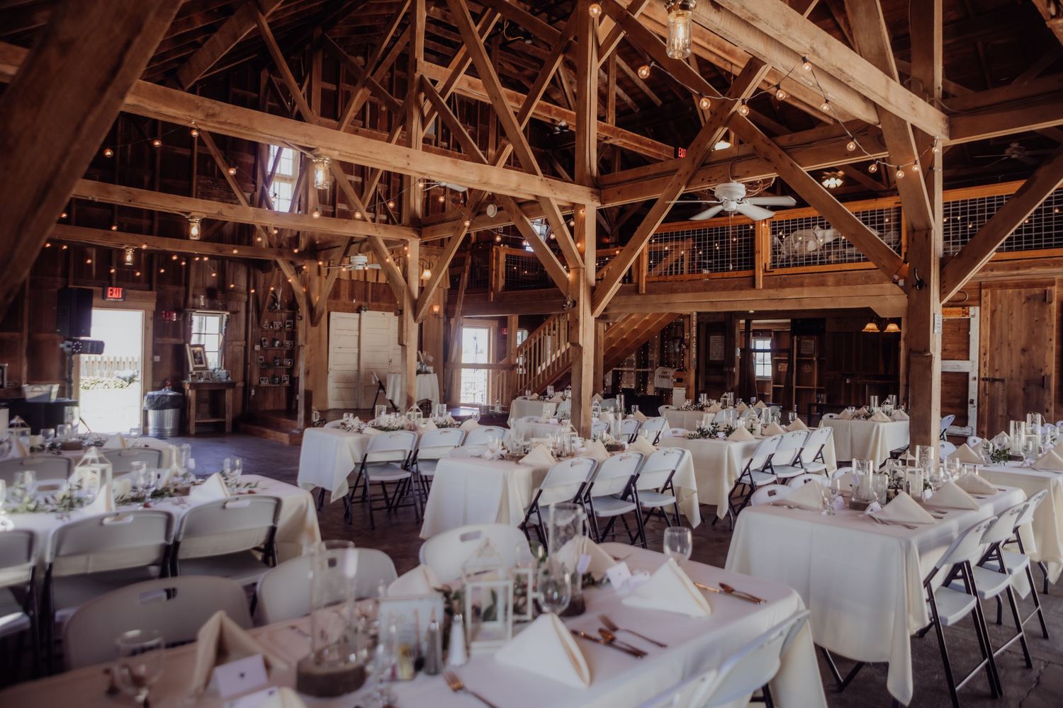 Rustic barn venue interior set up for a wedding reception with elegant white table settings and wooden beams.