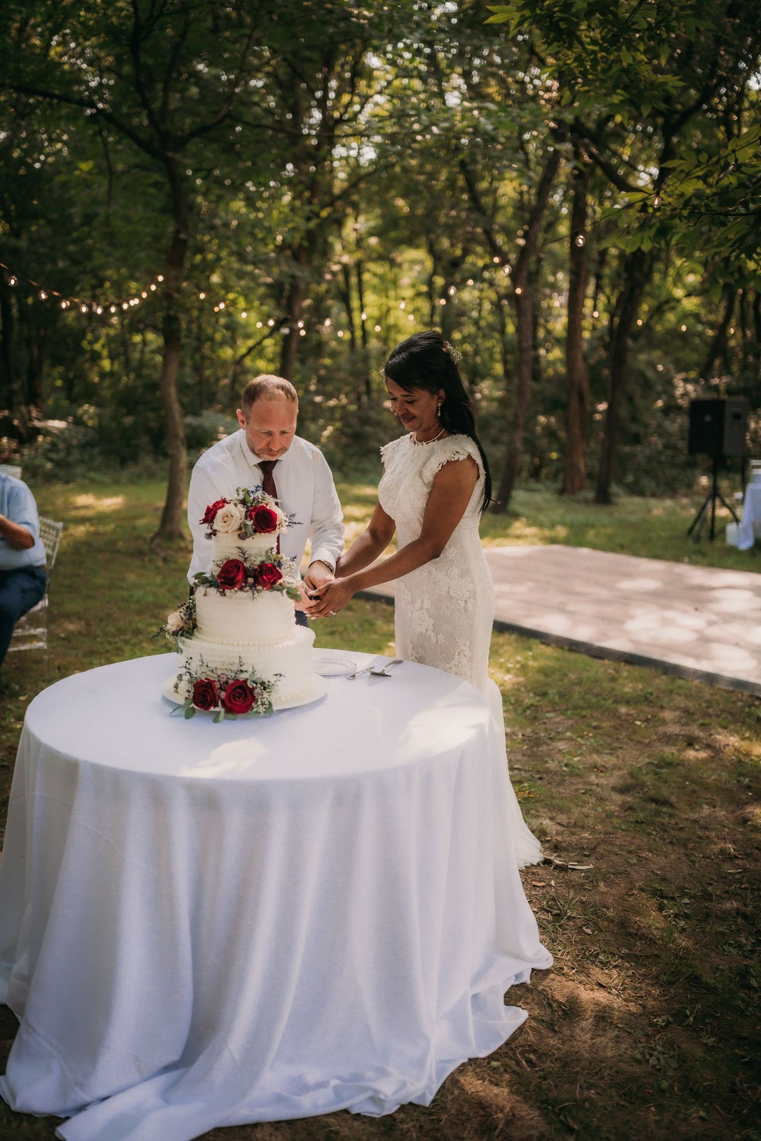 Wedding cake cutting moment at an elegant outdoor reception with white table linens.