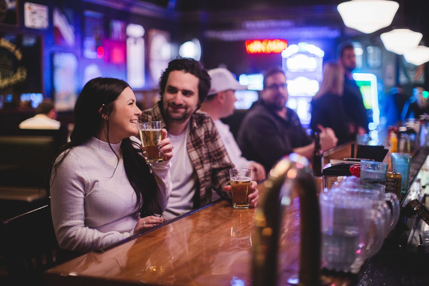 Friends chatting and drinking at a cozy neighborhood bar with purple ambient lighting.