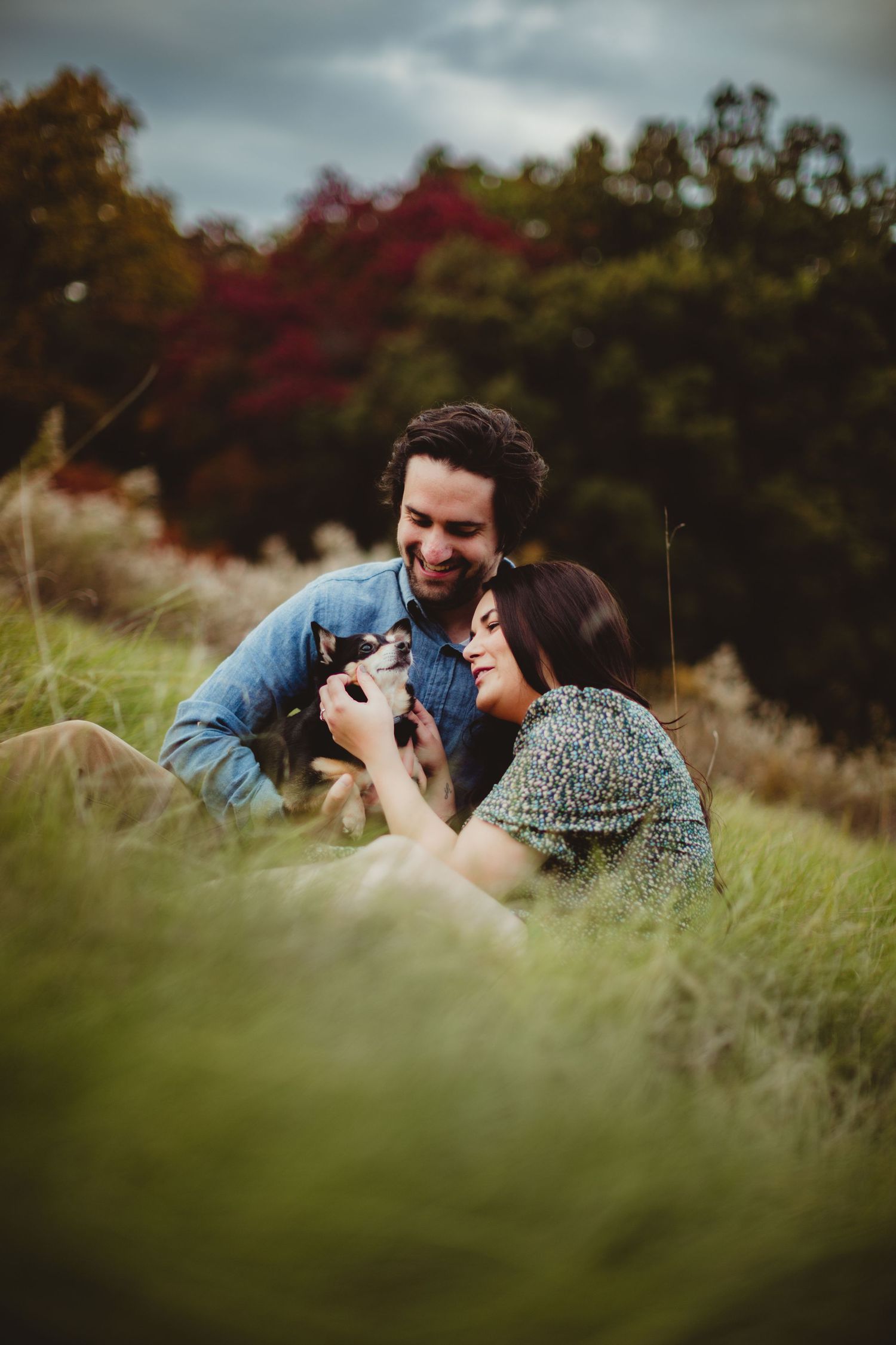 Couple laying in tall grass taking photos together during golden hour sunset.