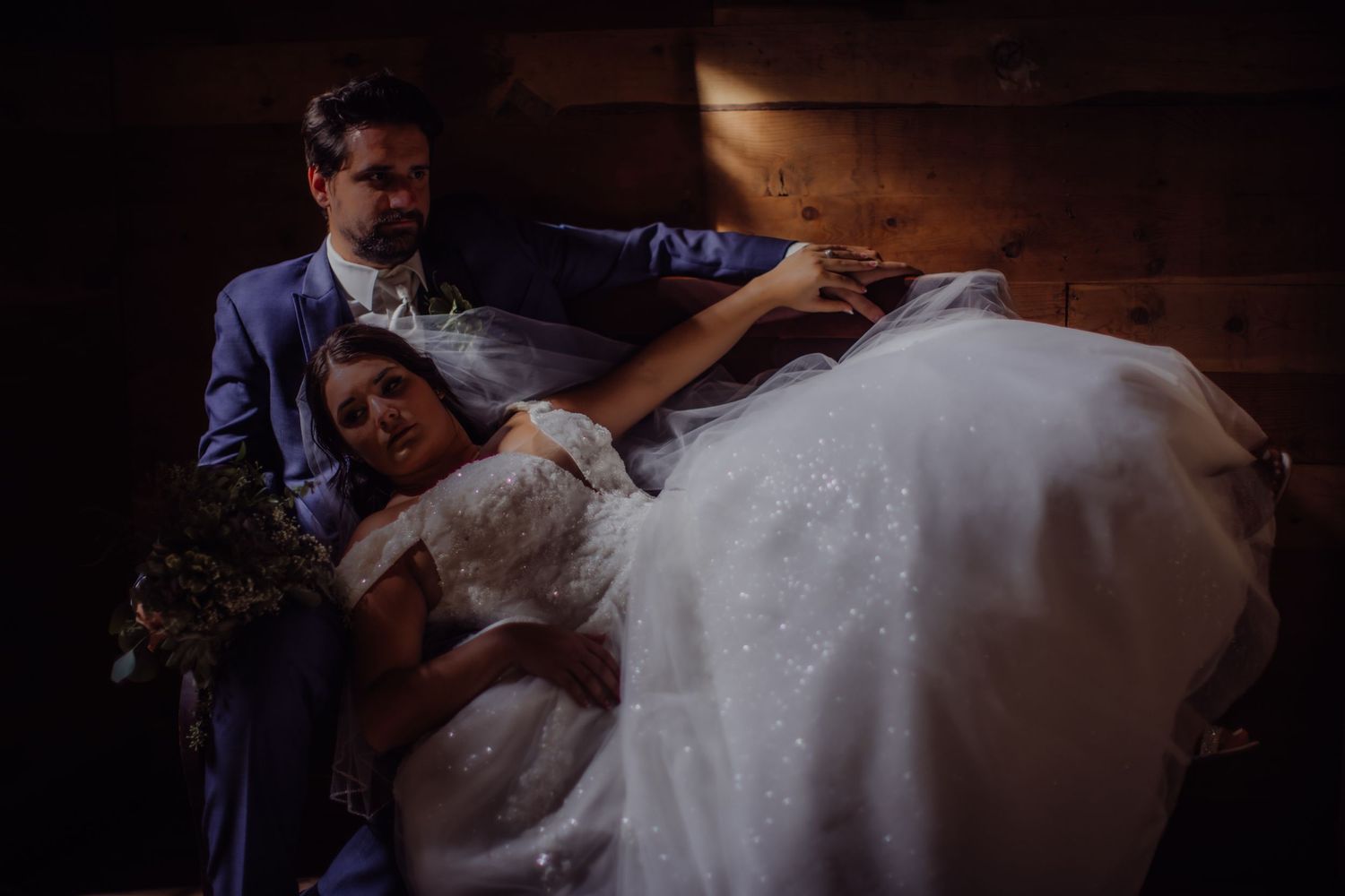 Moody wedding portrait with couple in dramatic lighting on wooden stairs.