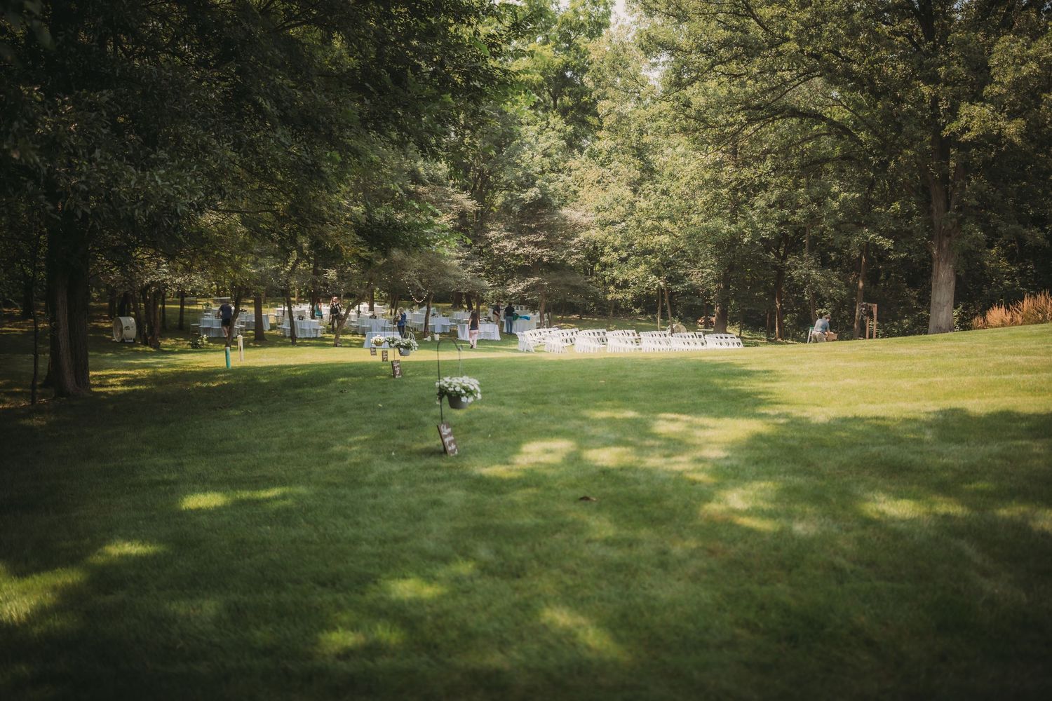 Sunlit outdoor wedding venue with white chairs set up on a lush green lawn.