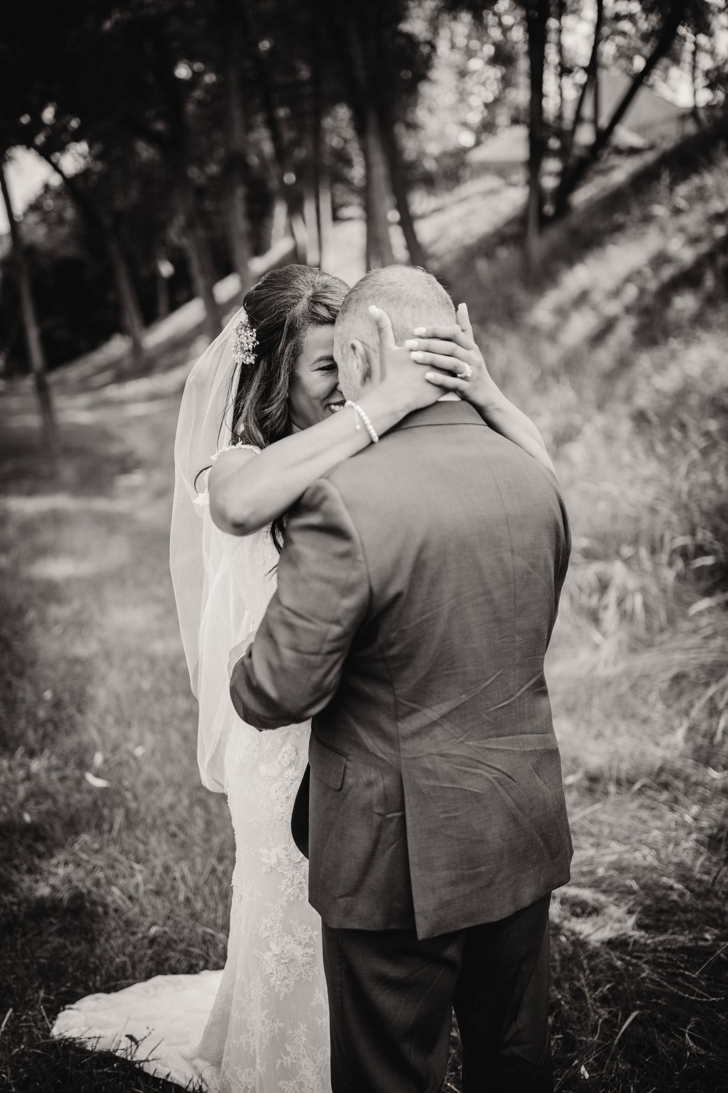 A tender black and white wedding moment captured in a wooded outdoor setting with natural lighting and romantic embrace.