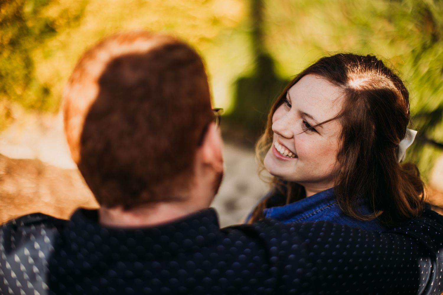 A couple shares an intimate moment outdoors with autumn foliage in the background.