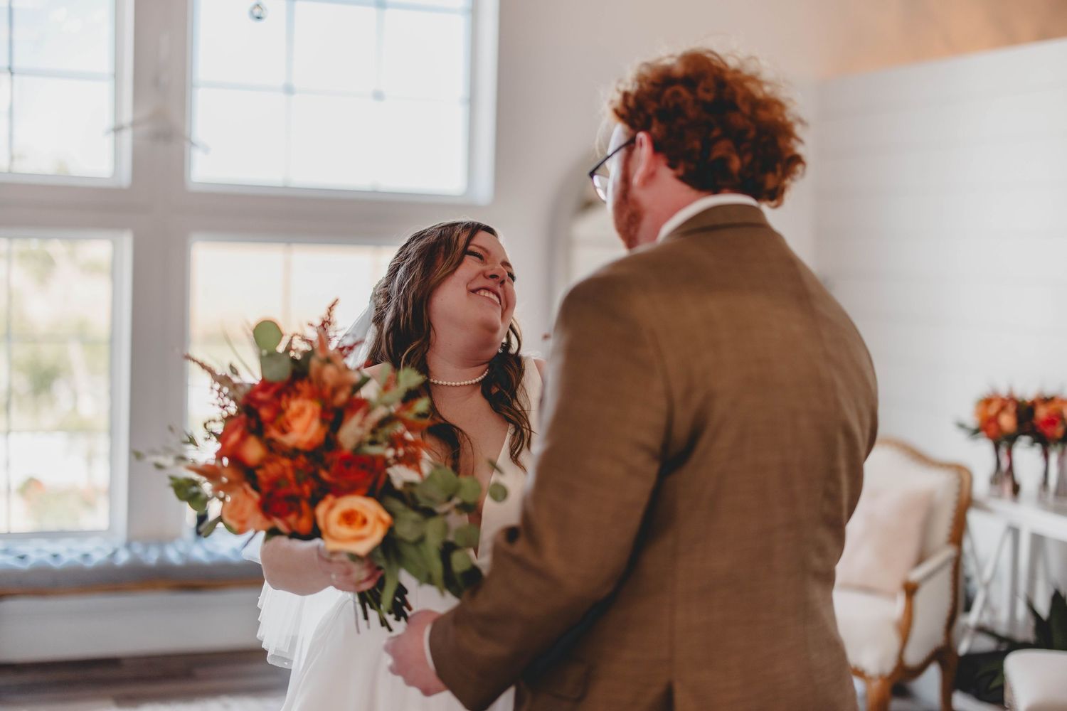 Romantic wedding moment captured in light-filled room with fall-themed florals.