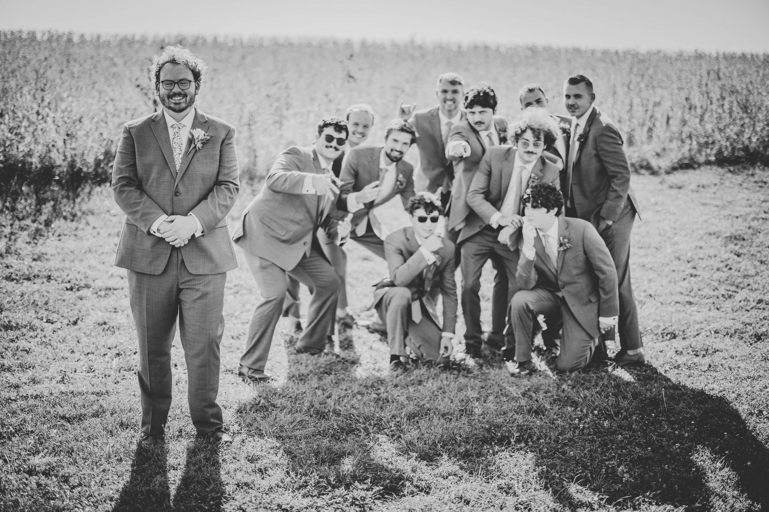 Black and white photo showcasing groomsmen striking fun poses in a rustic outdoor setting.