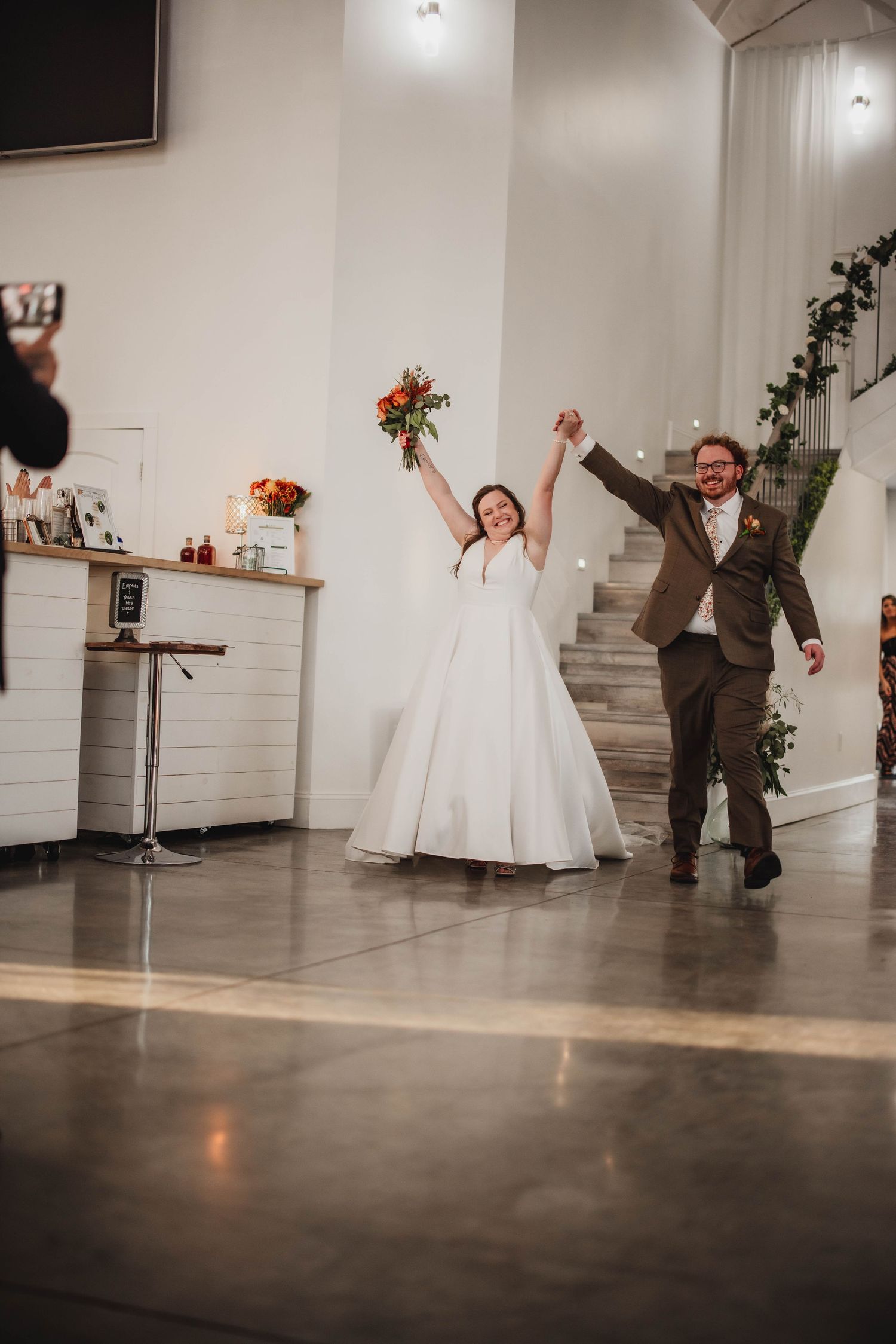 Happy newlyweds celebrate with raised arms and energetic movements during their wedding reception entrance.