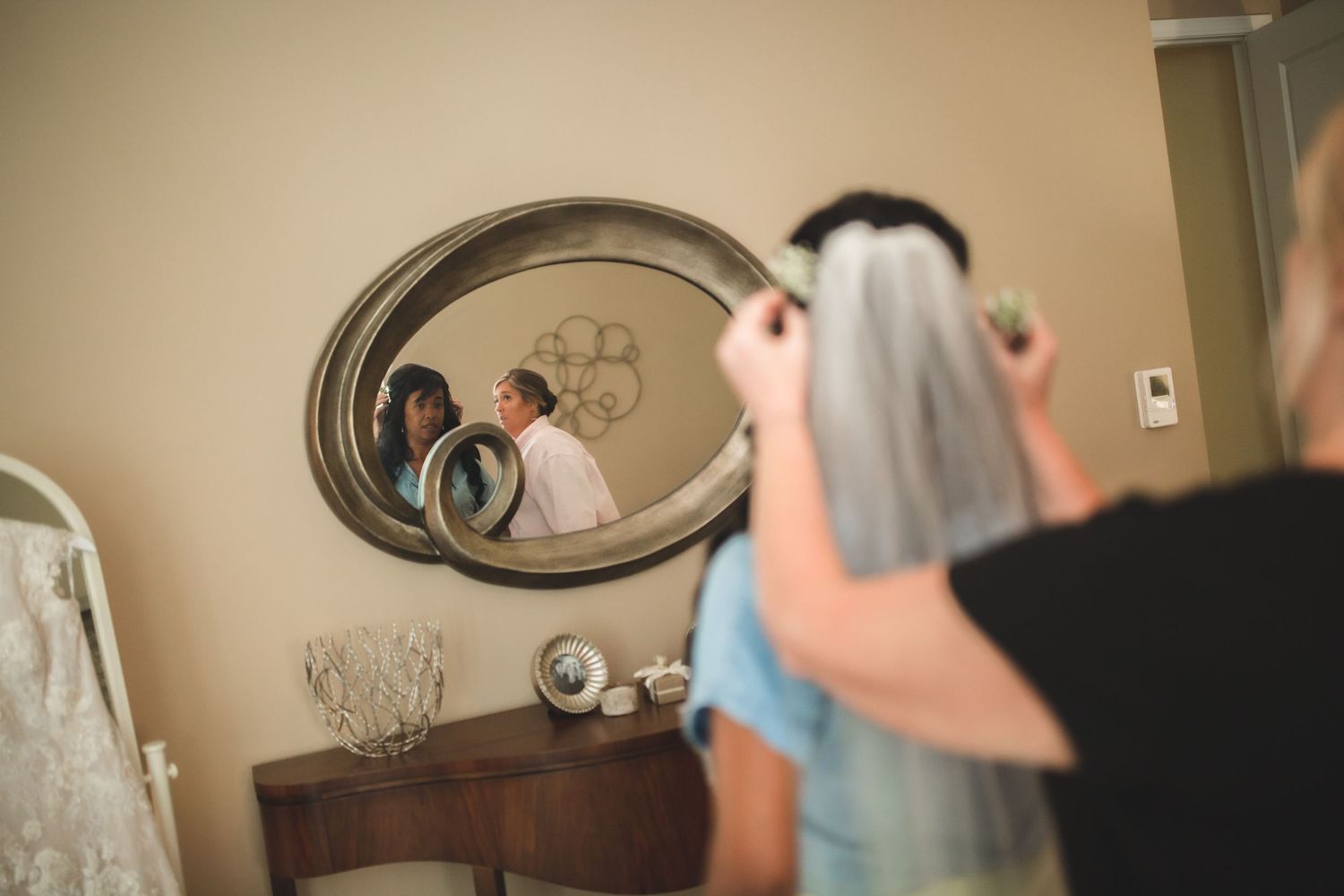 Artistic mirror shot captures wedding preparation scene with veil placement.