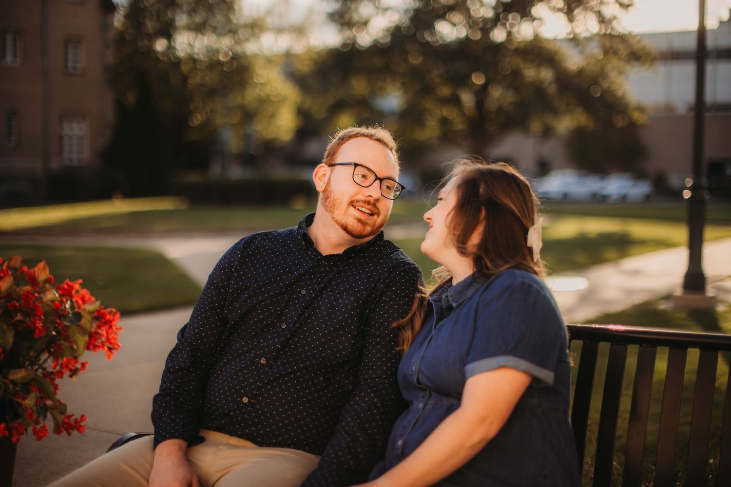 Couple sitting on park bench near red flowers during golden hour.