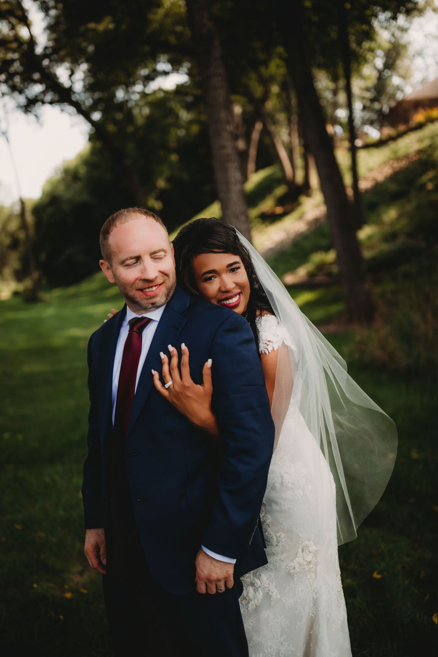 A happy couple embraces while taking wedding photos in a scenic wooded park.