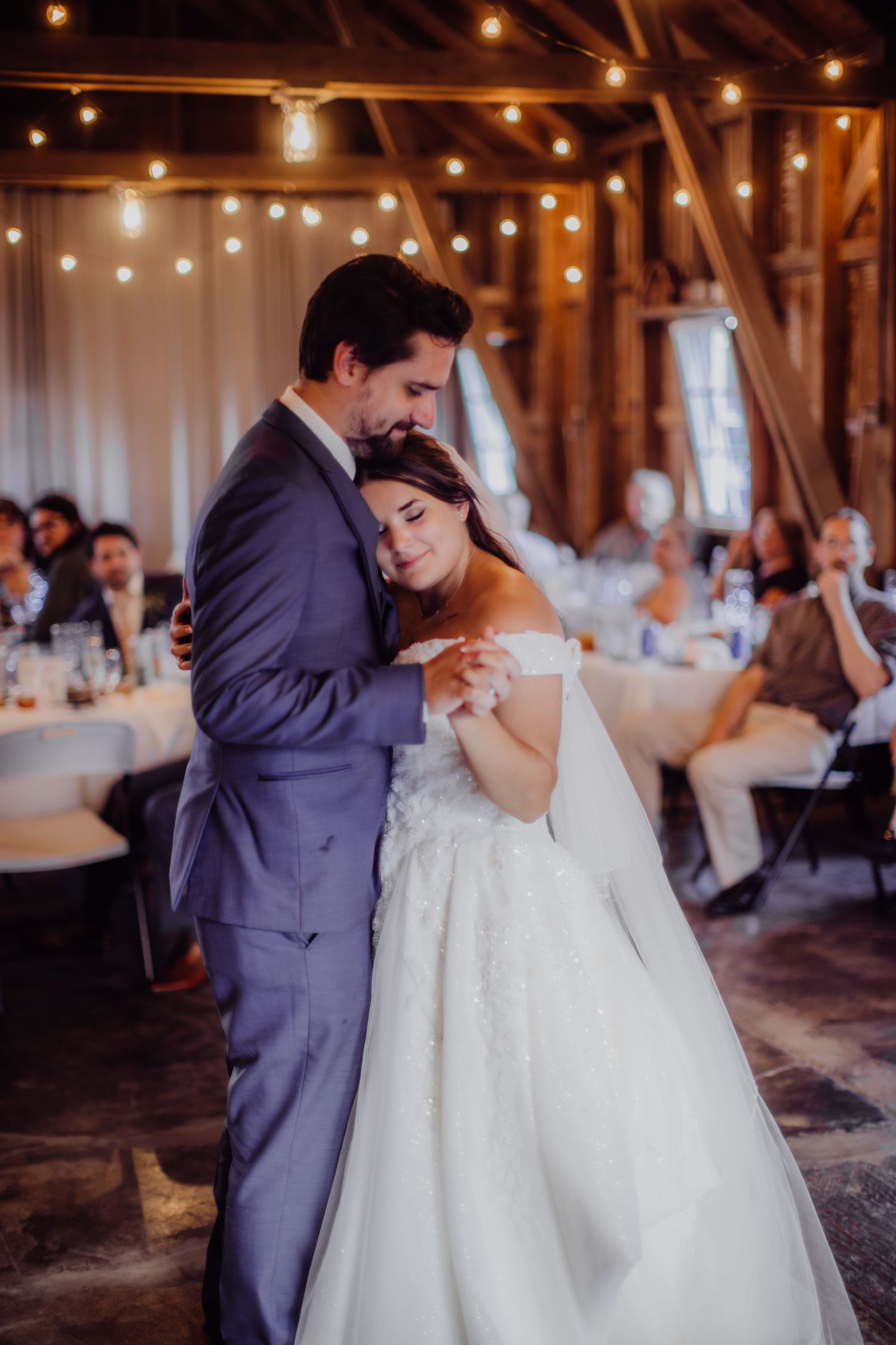 Romantic first dance moment in a rustic barn reception with ambient lighting.