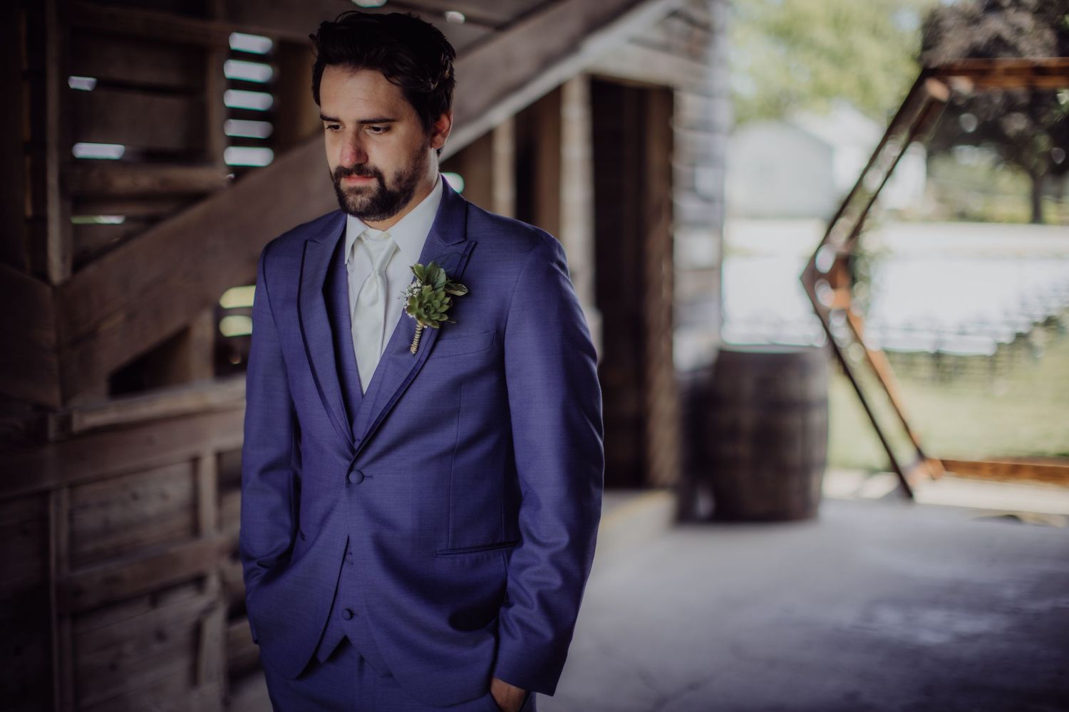 Groom in navy suit during first look photos in rustic barn setting.