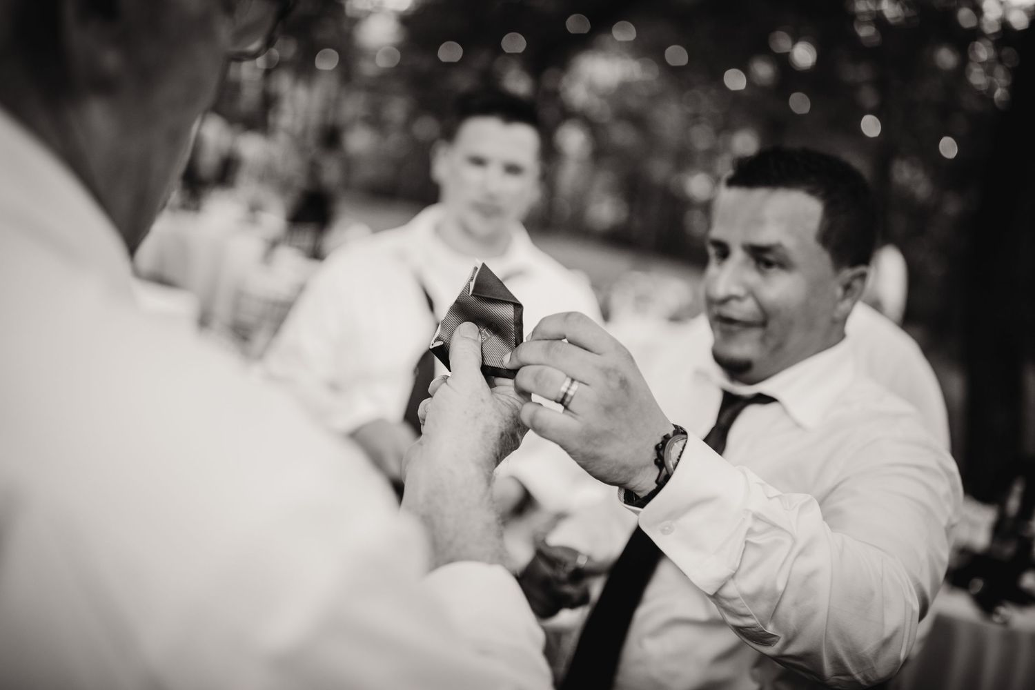 Black and white photo captures a joyful moment between wedding attendees outdoors.