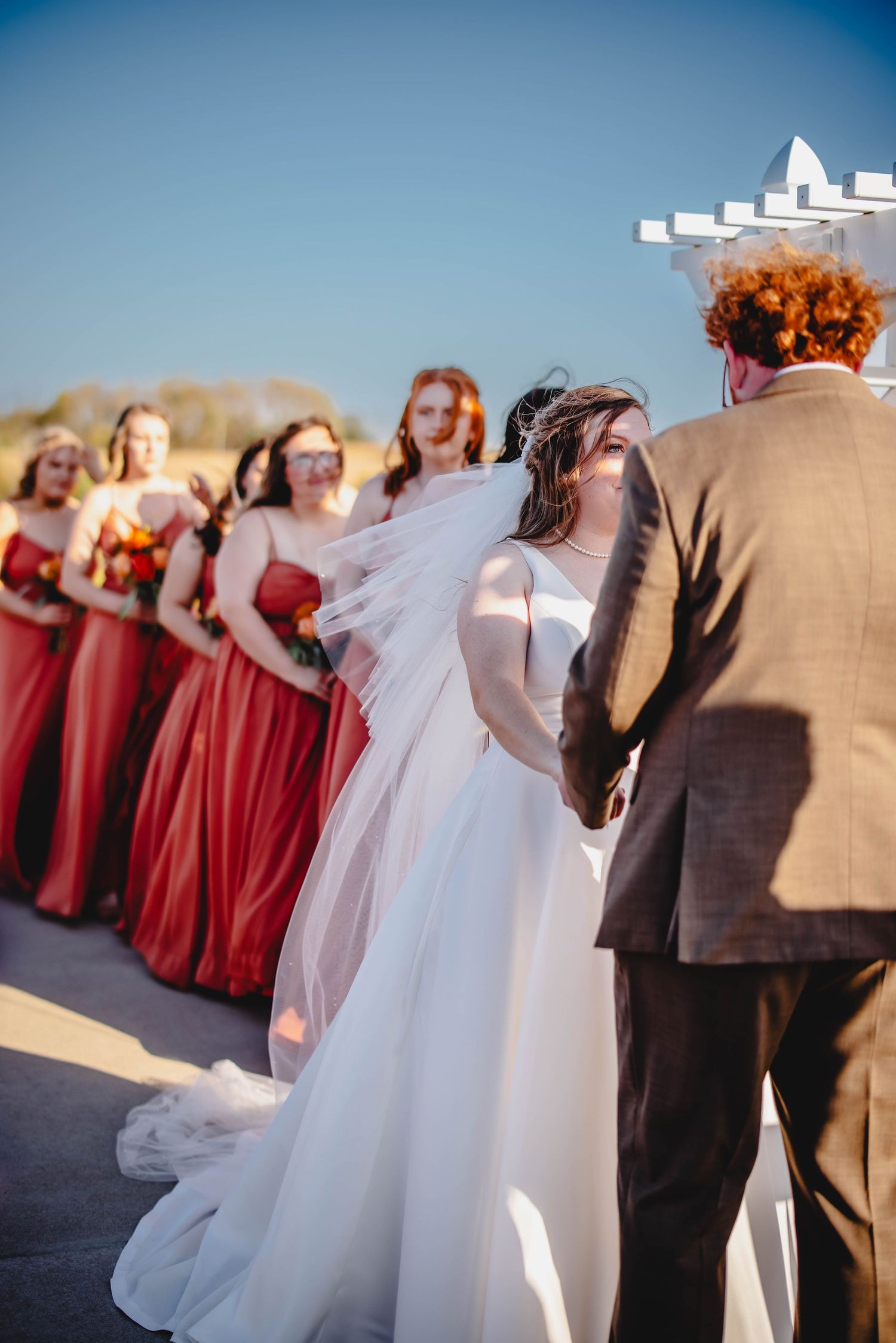 Wedding party in red bridesmaid dresses lined up during outdoor ceremony.