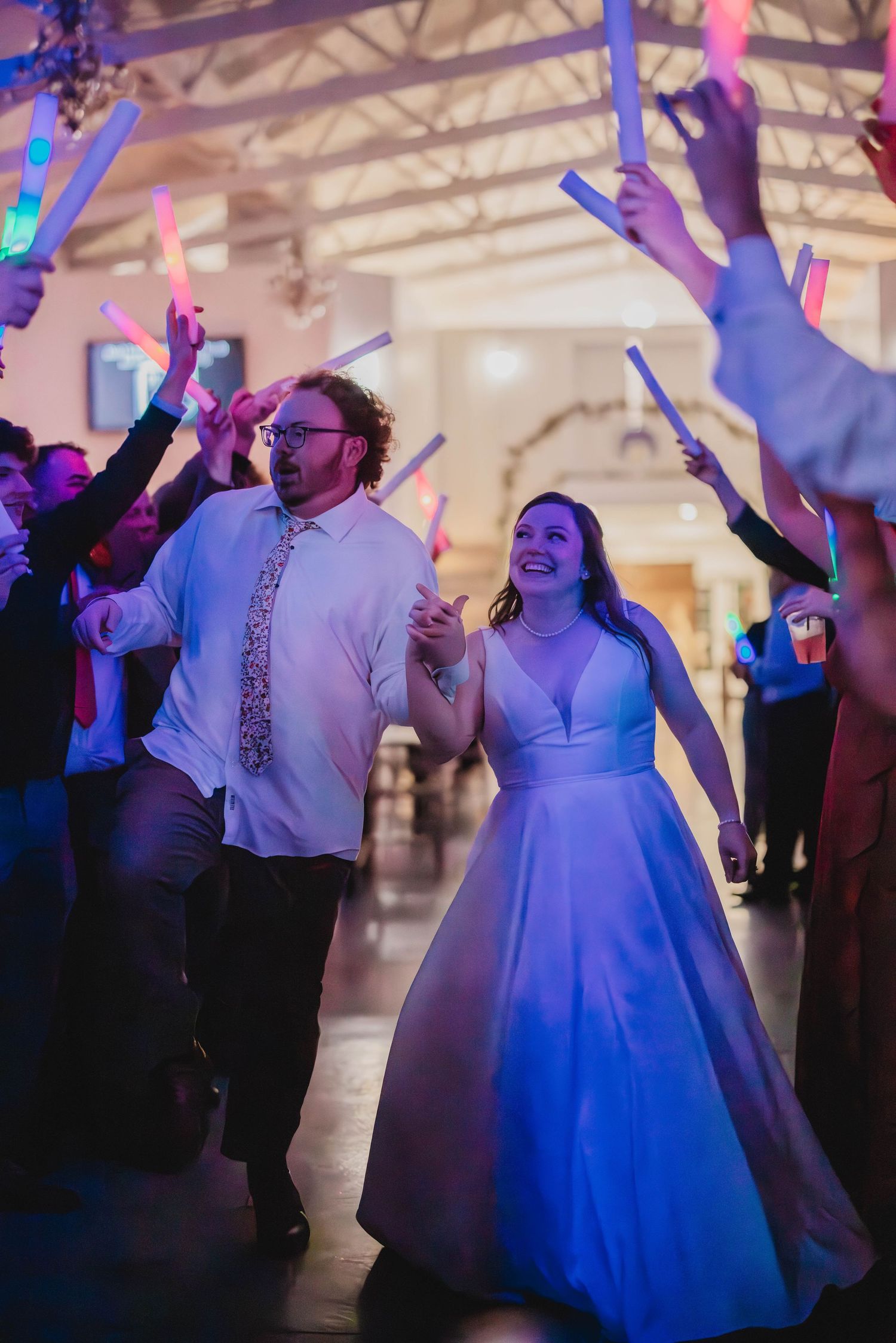 Wedding celebration features couple dancing under glowing light sticks held by guests.