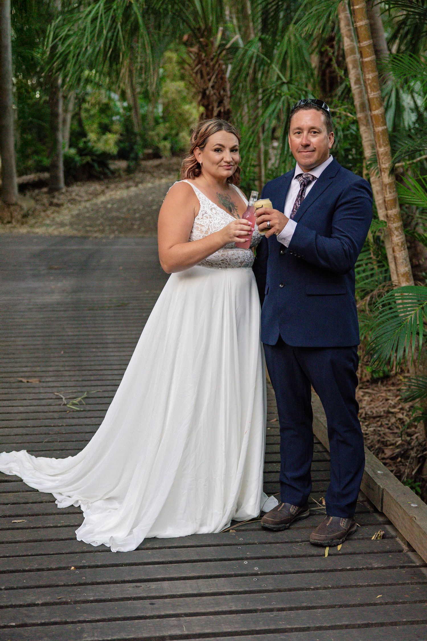 A couple stands together on a wooden boardwalk surrounded by palm trees during their outdoor wedding.