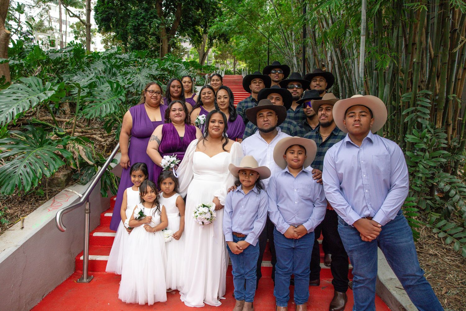 A group photo showing multiple people gathered outdoors in casual attire with trees and foliage visible in the background.