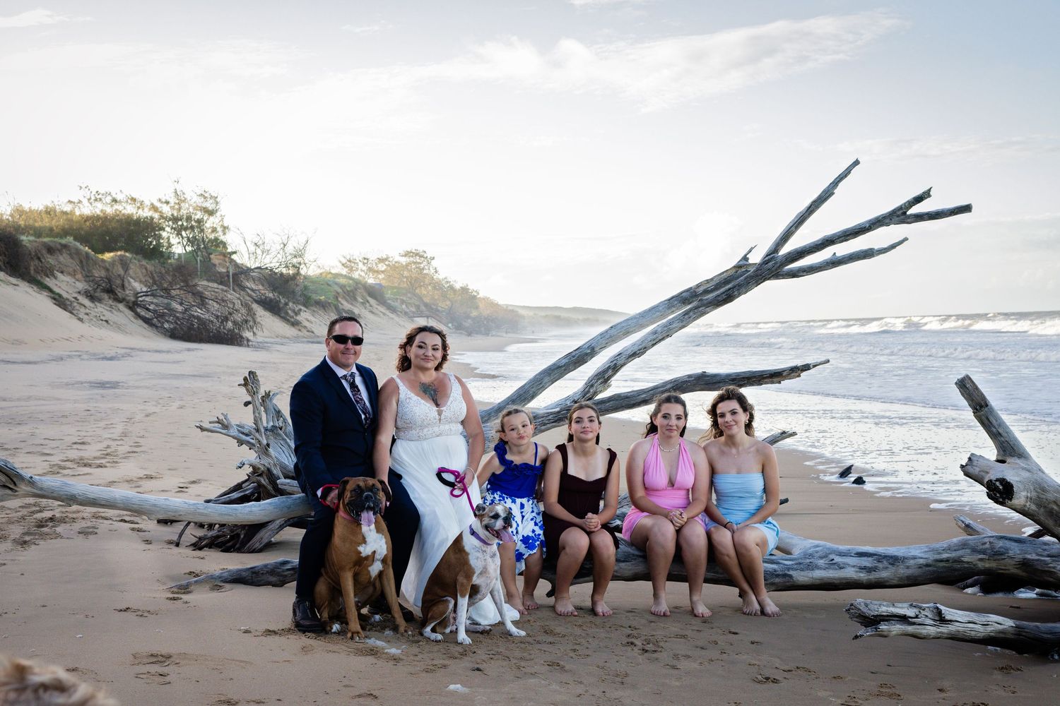 Group gathered on a beach at sunset with driftwood and ocean waves in the background.