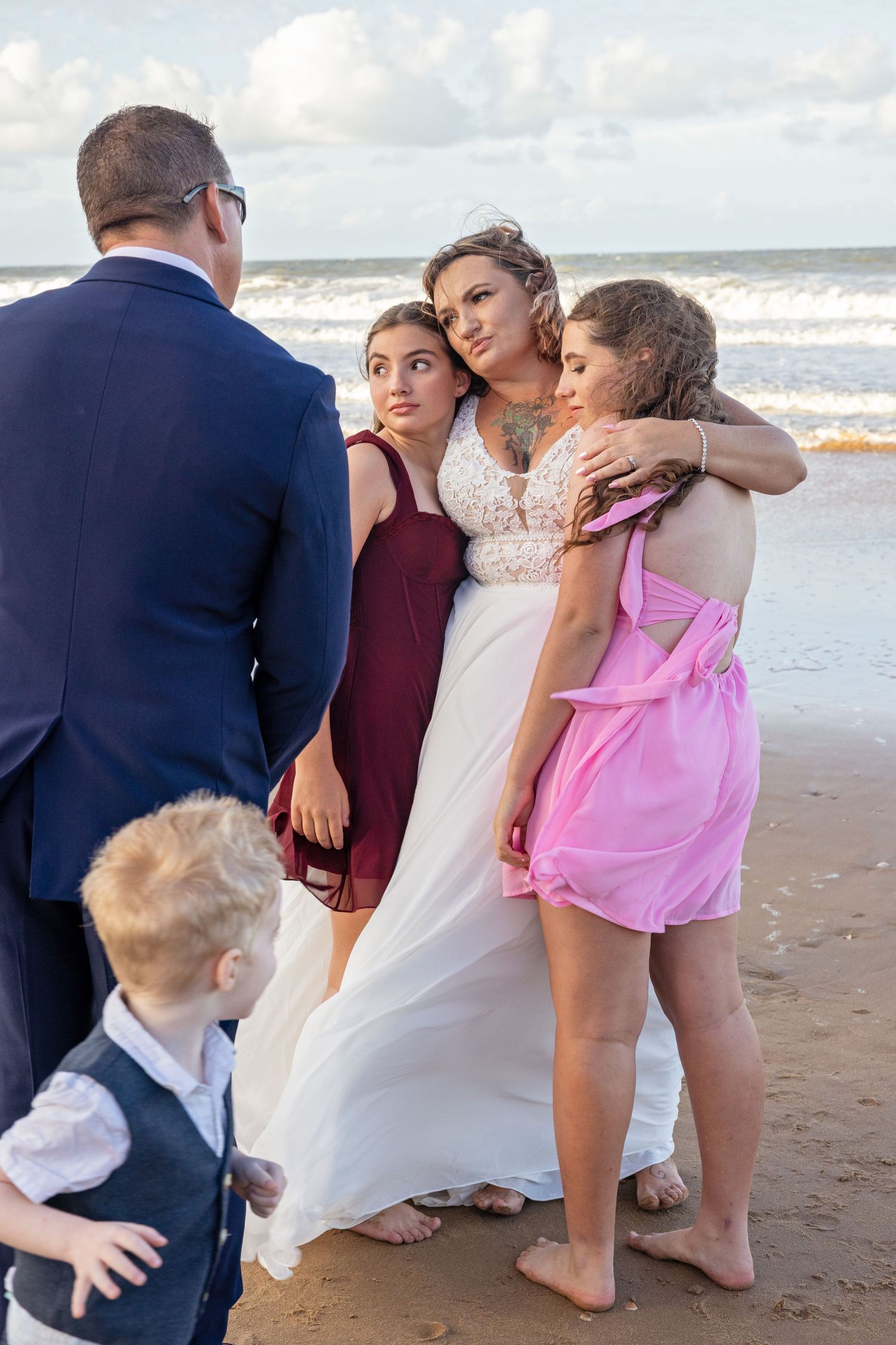 Wedding group posing together on a beach with waves and cloudy sky in the background.