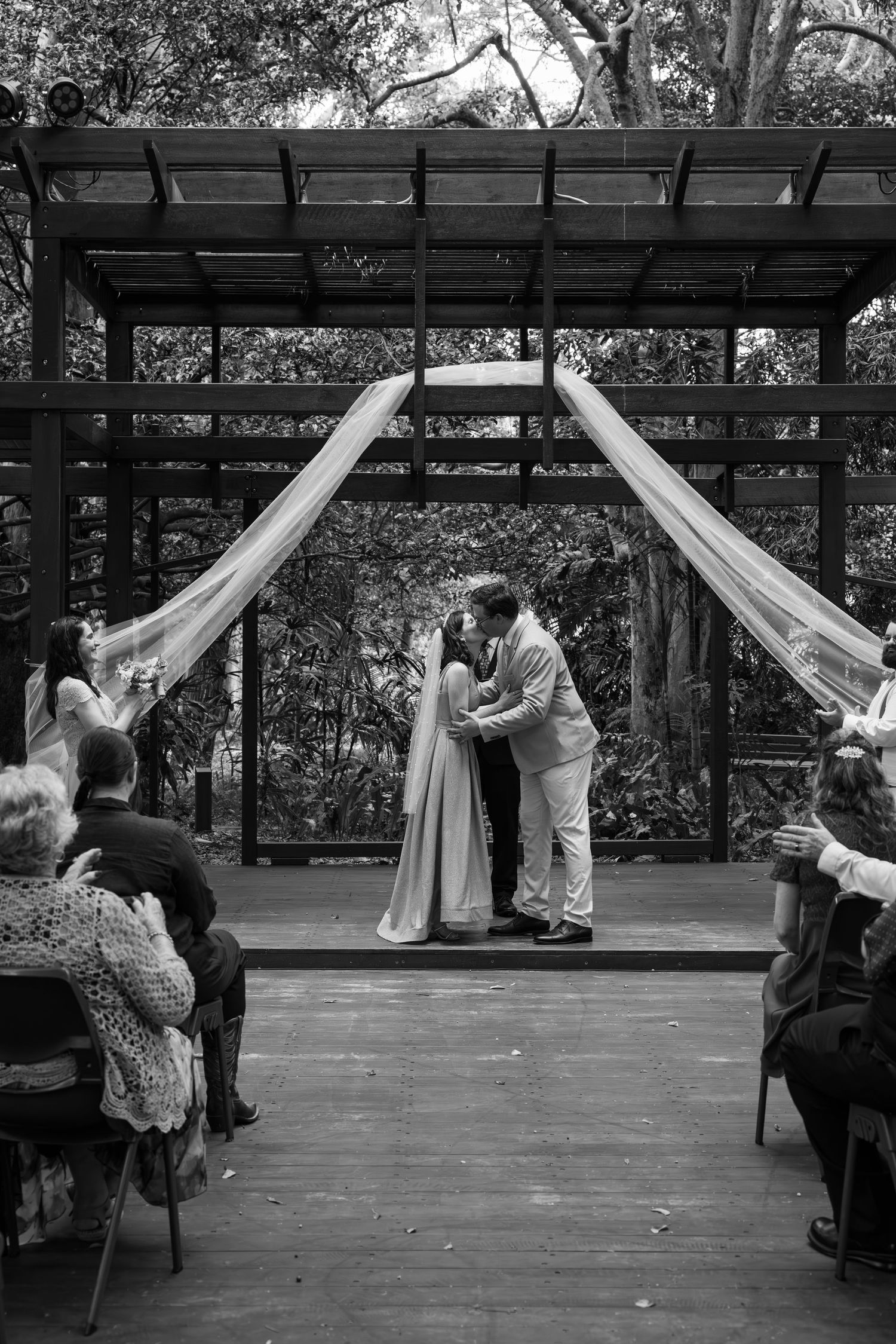 Wedding ceremony under draped pergola with guests seated on outdoor deck.