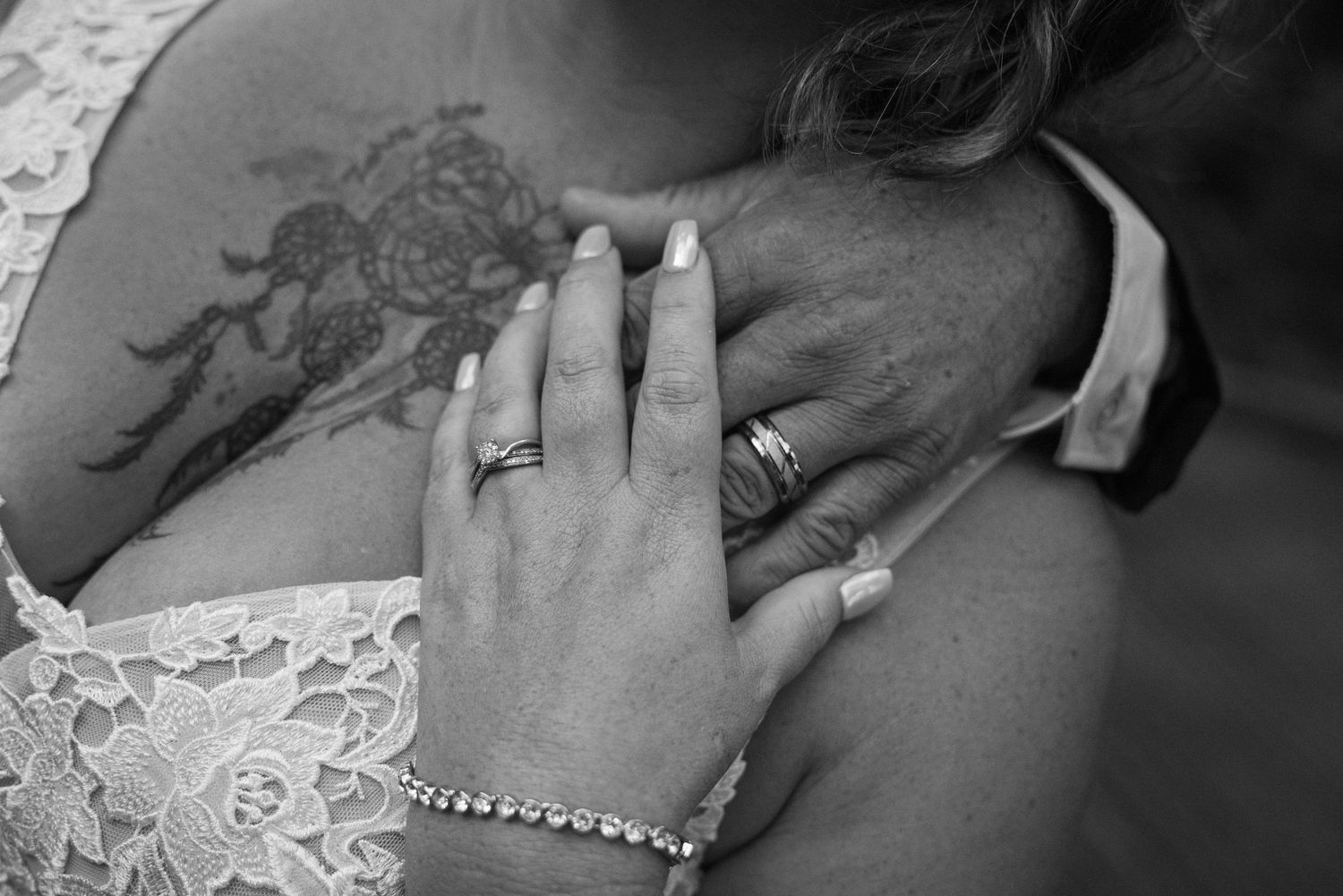 Black and white close up of hands embracing showing wedding rings and a lace dress detail.