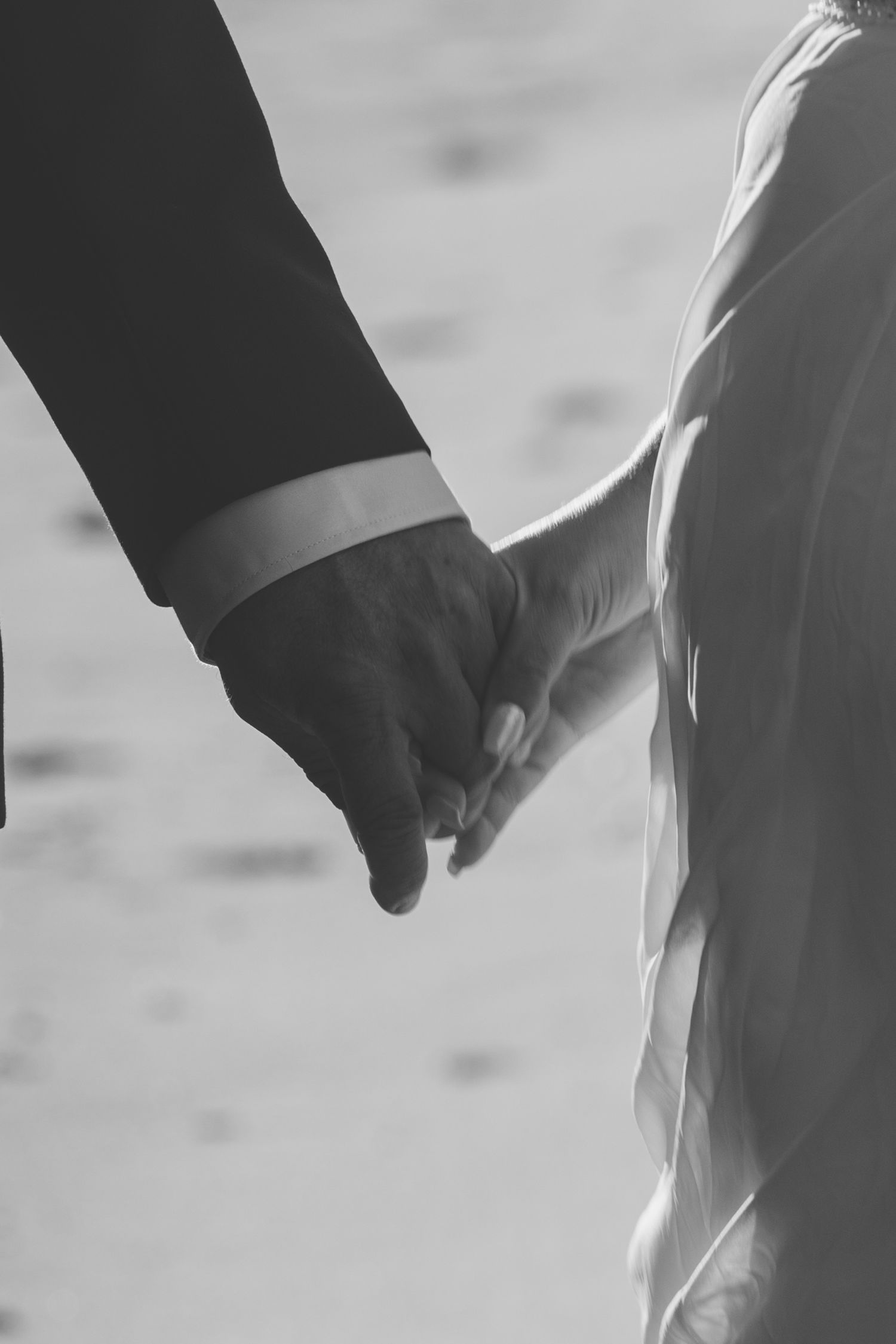 Two people walk together holding hands in a simple black and white photograph.