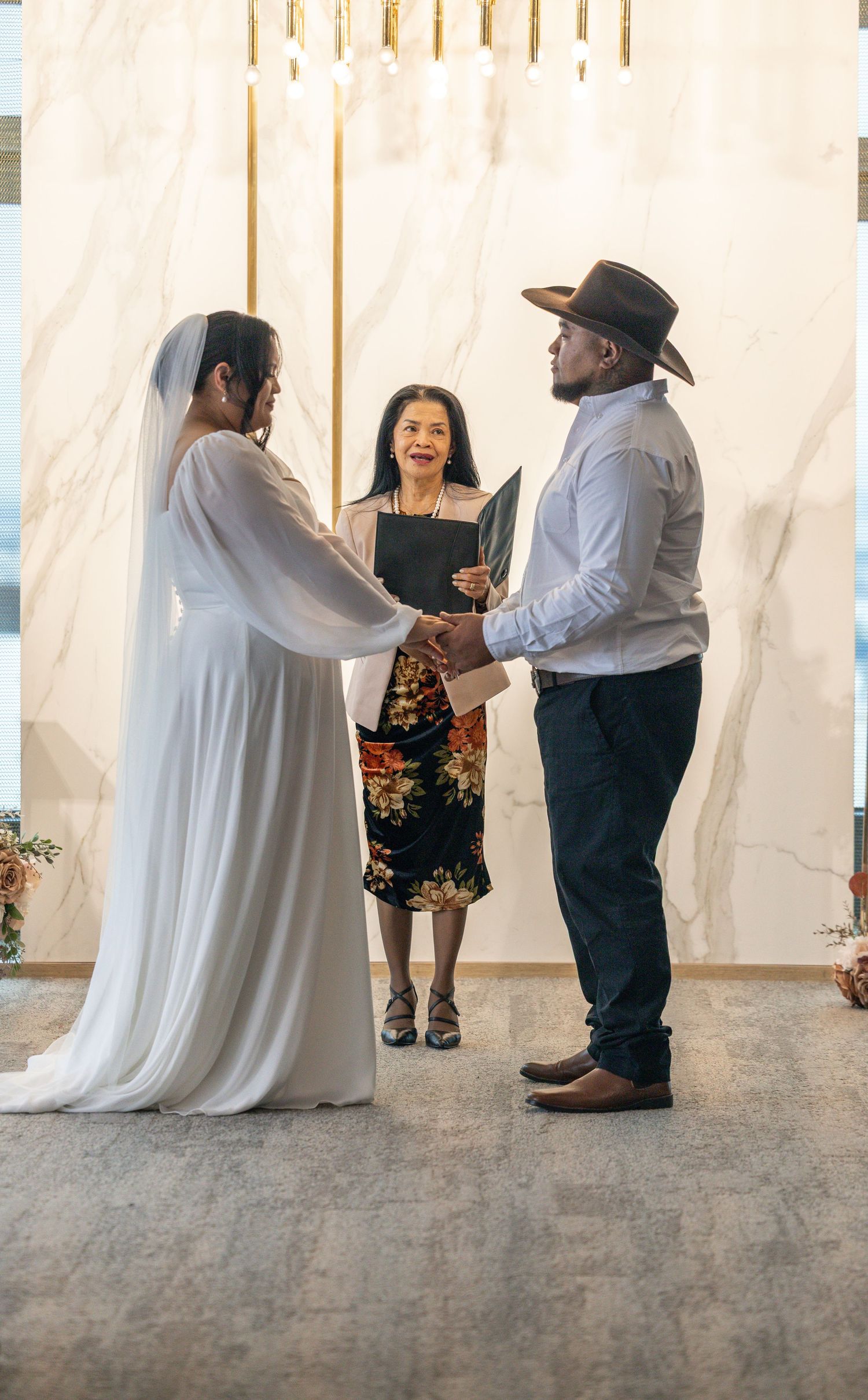 Wedding ceremony with an officiant in floral dress presiding over a couple's union under white draped fabric.